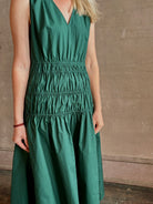 Mature woman wearing Loren Dress from Proenza Schouler White Lable rendered in aspruce green and crafted from a cotton elastane blend with v-neck, sleeveless, pockets, and rushed waist