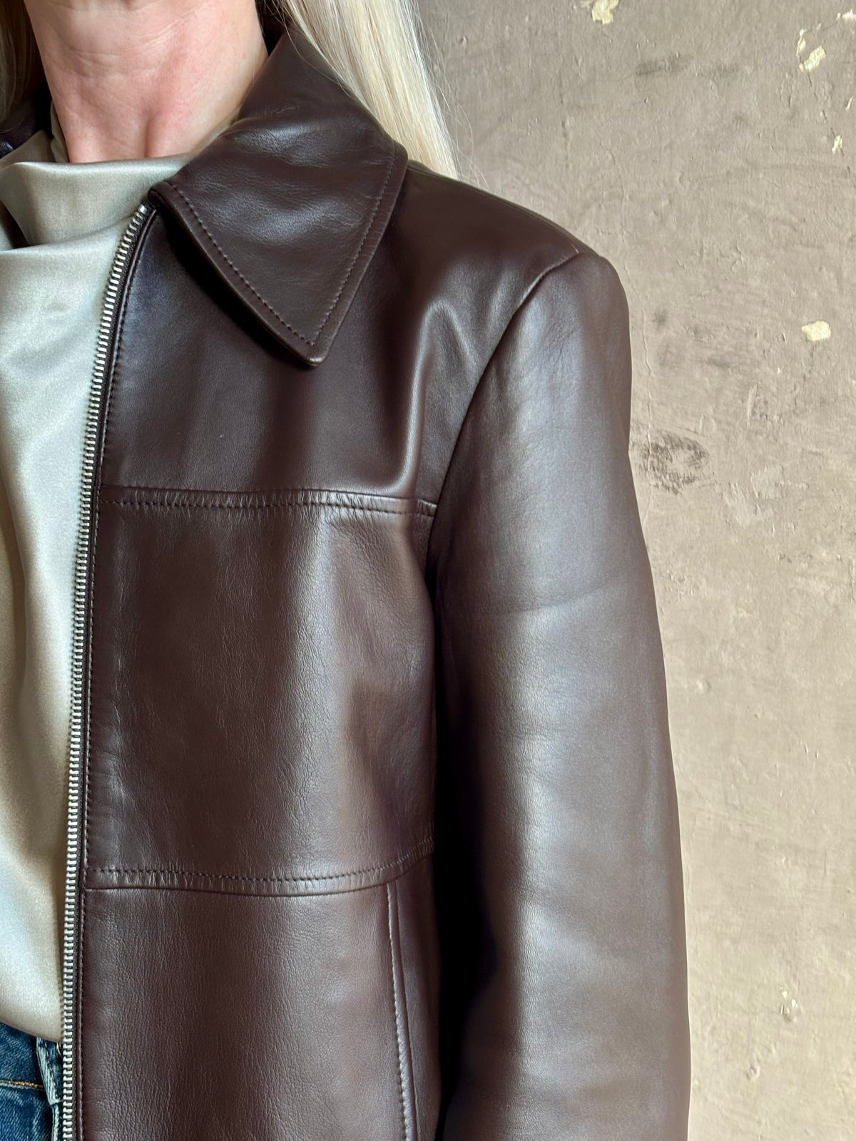 Close up image of mature woman wearing Proenza Schouler White Label Annabel Leather Jacket in Chocolate Brown with intricate seam details on front of jacket that wrap around the back
