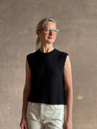 Mature woman wearing Rachel Comey designer Relent sleeveless black cotton knit top with a scalloped edges 
