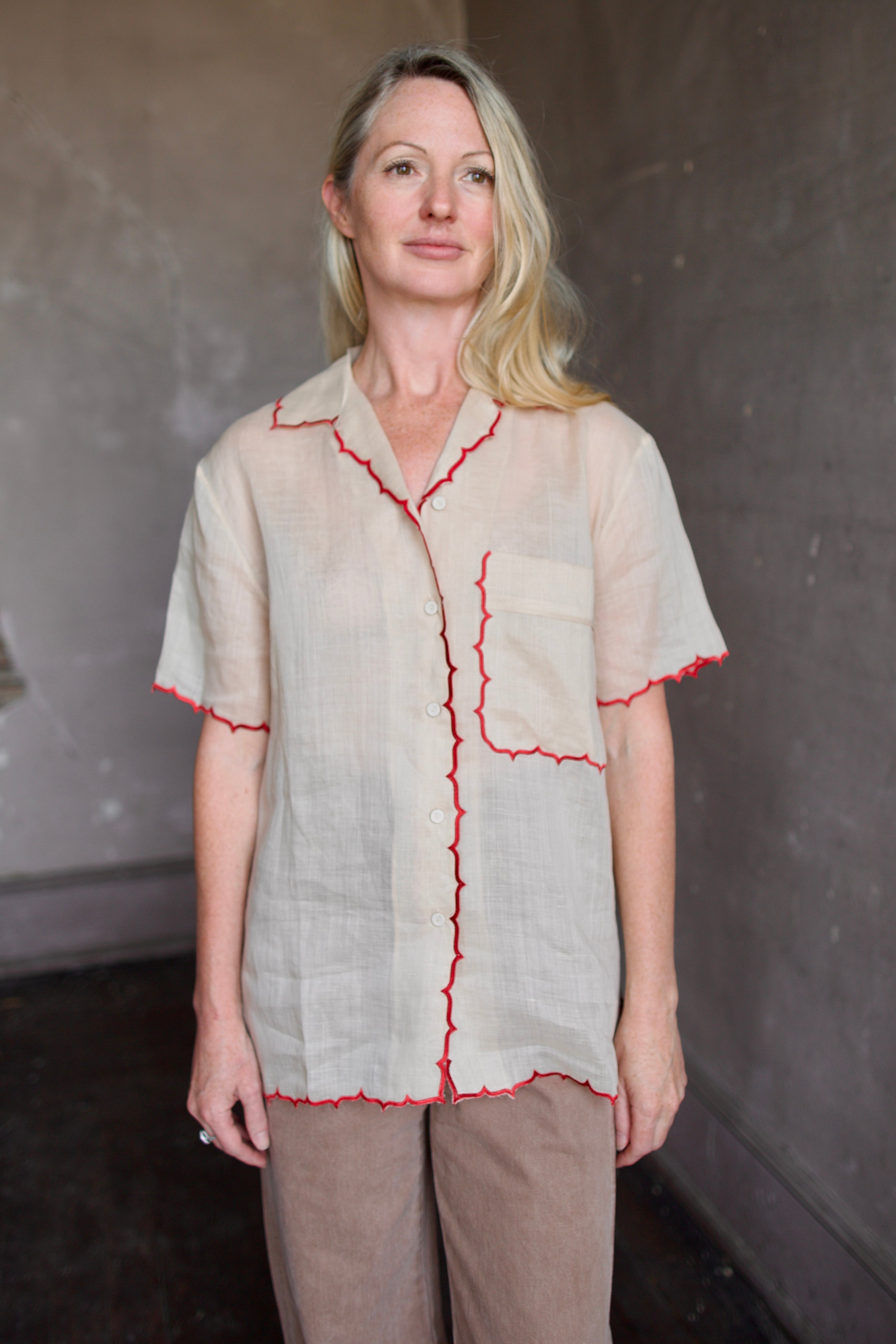 Model wearing a beige retro inspired blouse with scalloped red trim by Rachel Comey in raimey