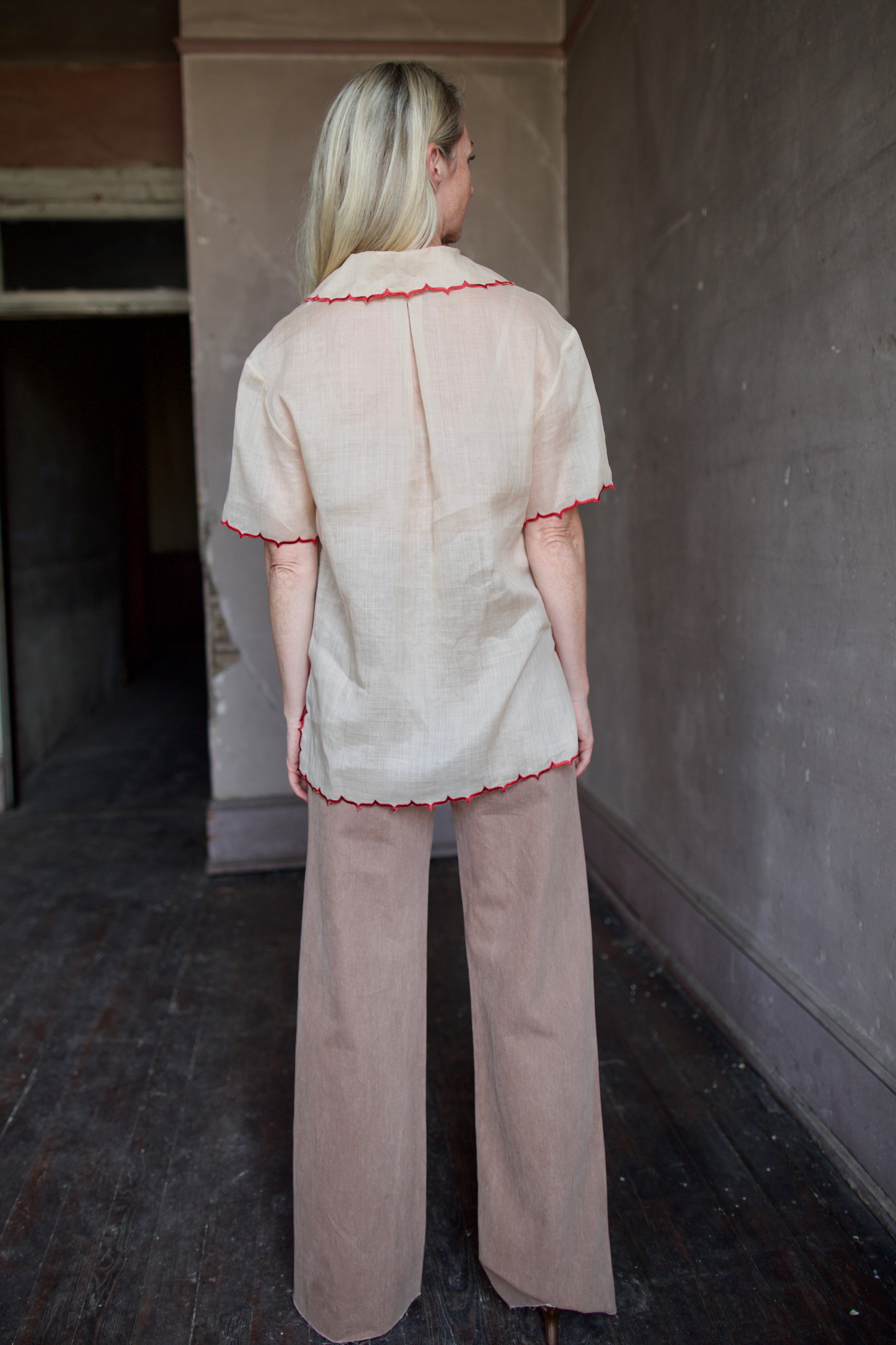 Model wearing a beige retro inspired blouse with scalloped red trim by Rachel Comey in raimey