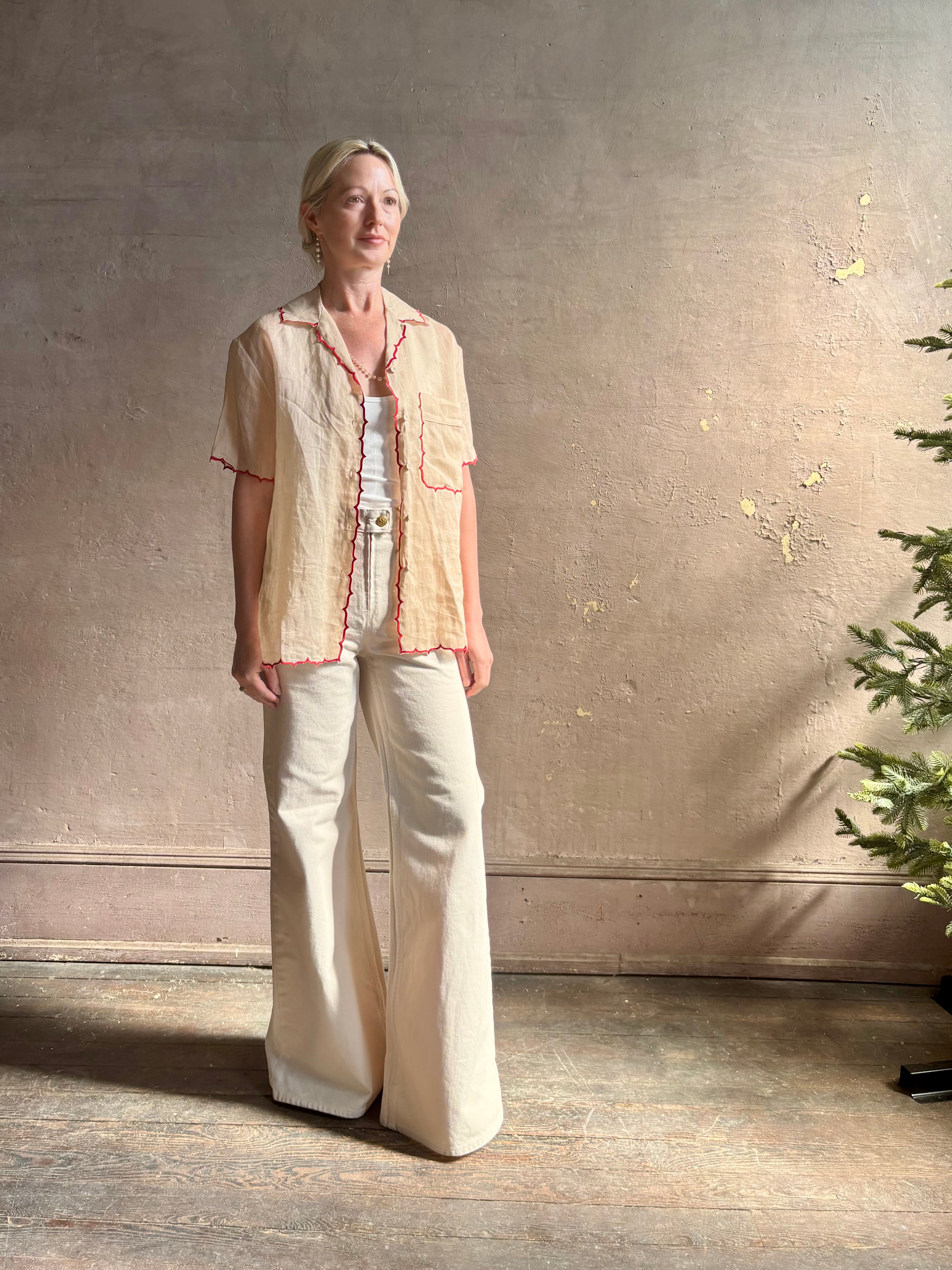 Mature woman wearing a beige retro inspired blouse with scalloped red trim by New York based Women's clothing designer Rachel Comey in raimey