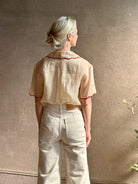 Mature woman wearing a beige retro inspired blouse with scalloped red trim by New York based Women's clothing designer Rachel Comey in raimey