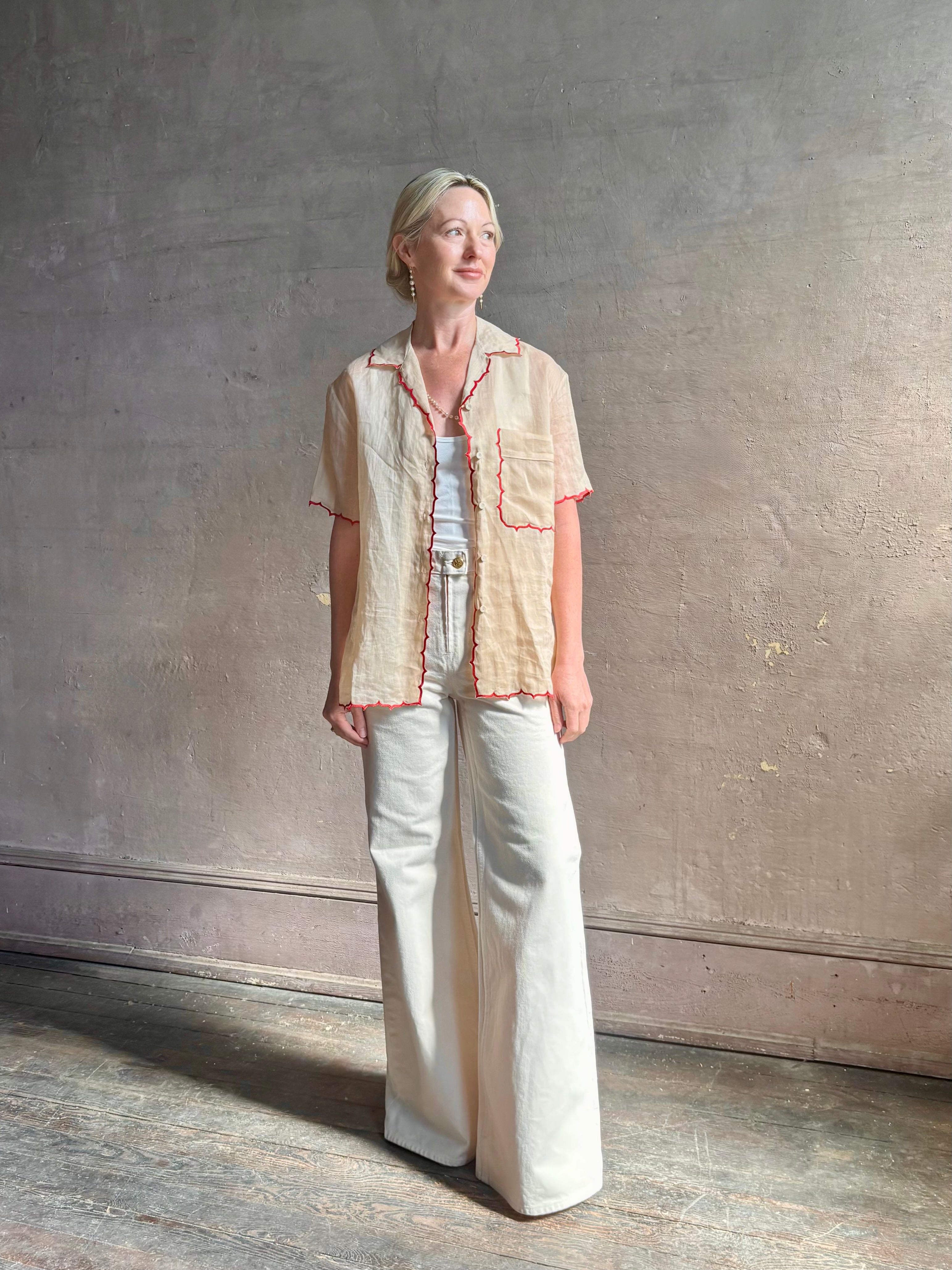 Mature woman wearing a beige retro inspired blouse with scalloped red trim by New York based Women's clothing designer Rachel Comey in raimey