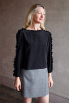 Mature model wearing a Rachel Comey black blouse with ruffled trim and an Apiece Apart gray wool skirt 