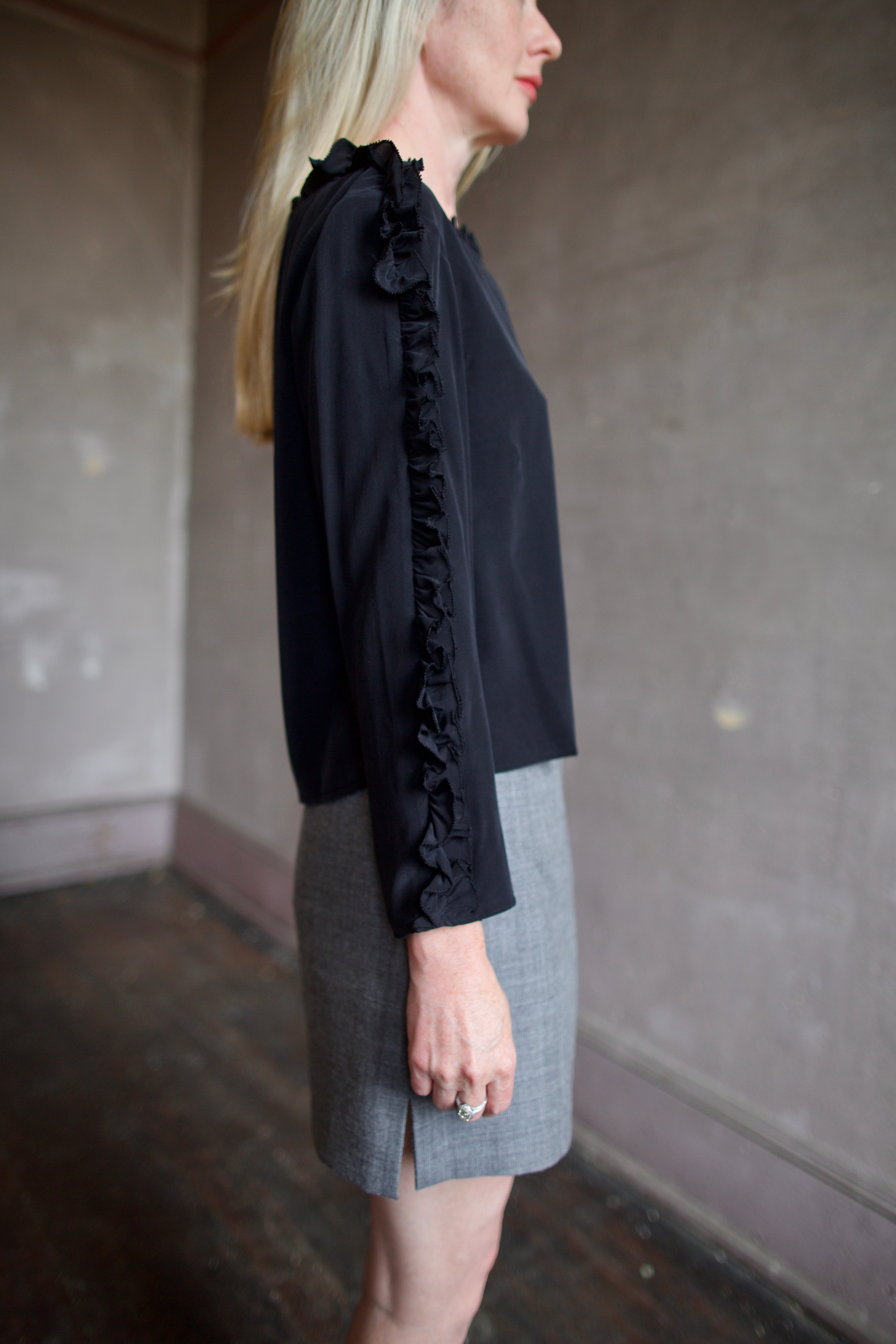 Mature model wearing a Rachel Comey black blouse with ruffled trim and an Apiece Apart gray wool skirt 
