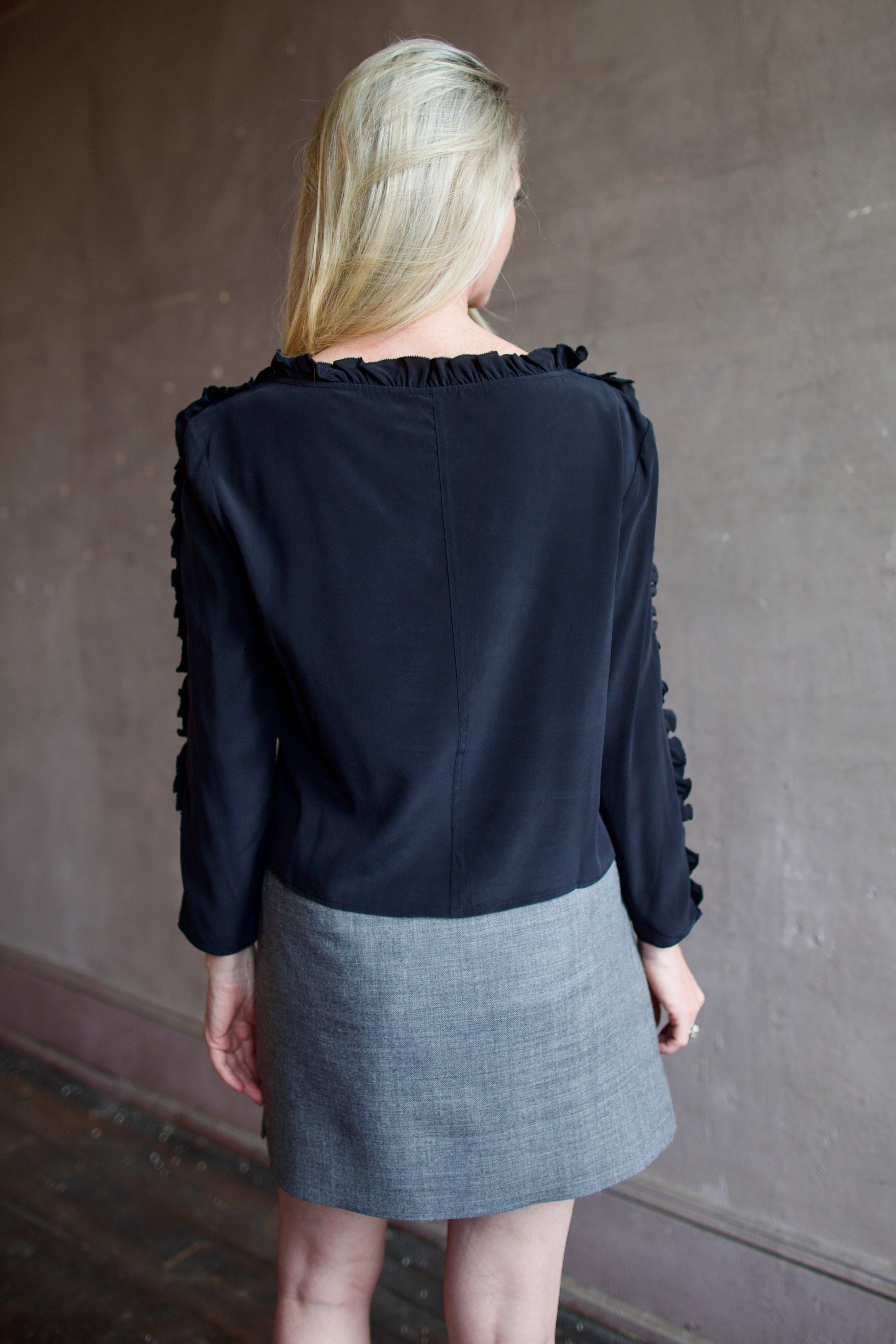 Mature model wearing a Rachel Comey black blouse with ruffled trim and an Apiece Apart gray wool skirt 