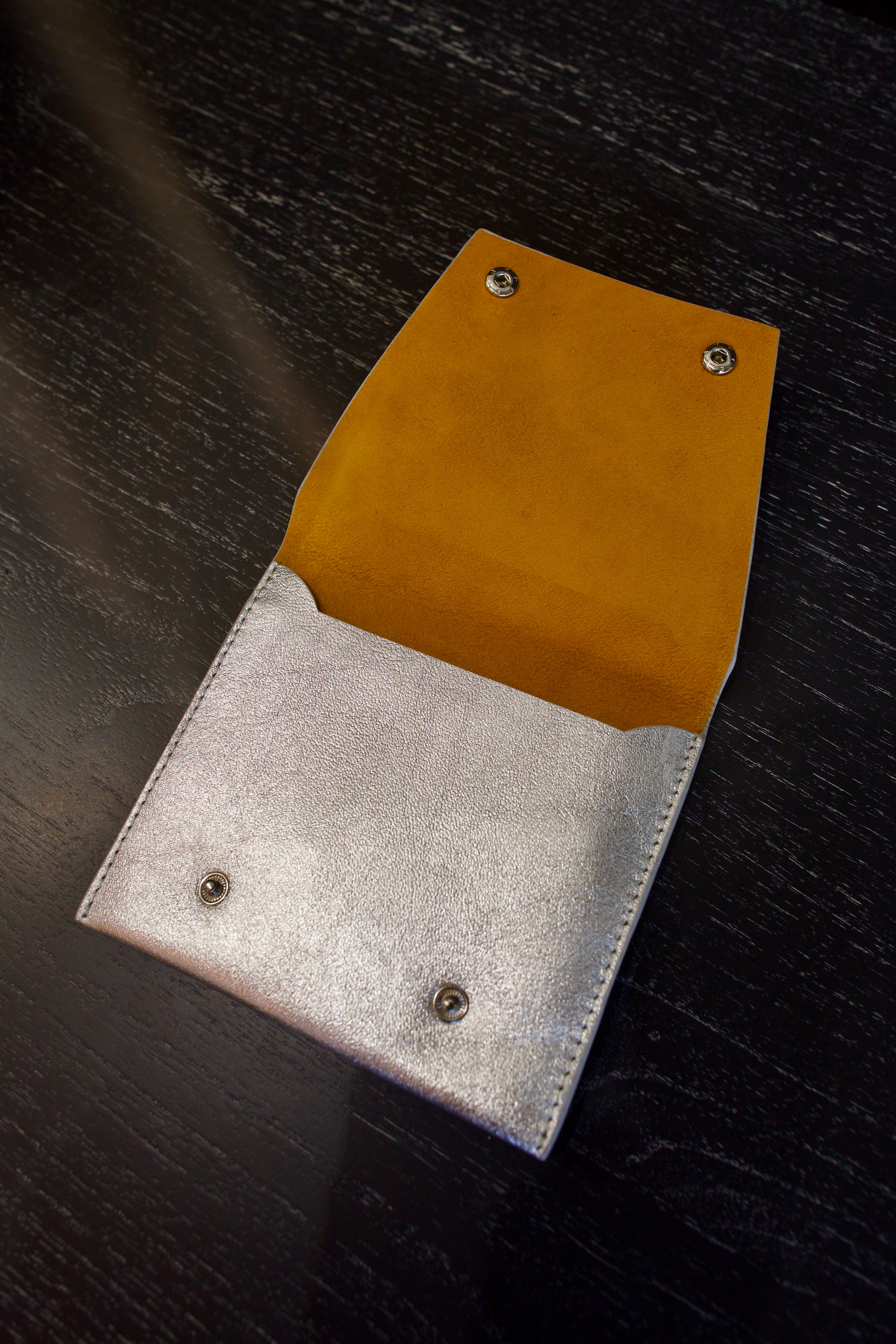 Photo of a silver metallic Rachel Comey leather wallet open with two snap buttons closure