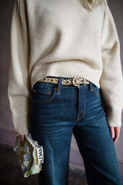 Image of a woman wearing the Rag & Bone Aria taupe leather-wrapped gold metal belt gives dimension to this belt, featuring a rounded pin buckle closure.