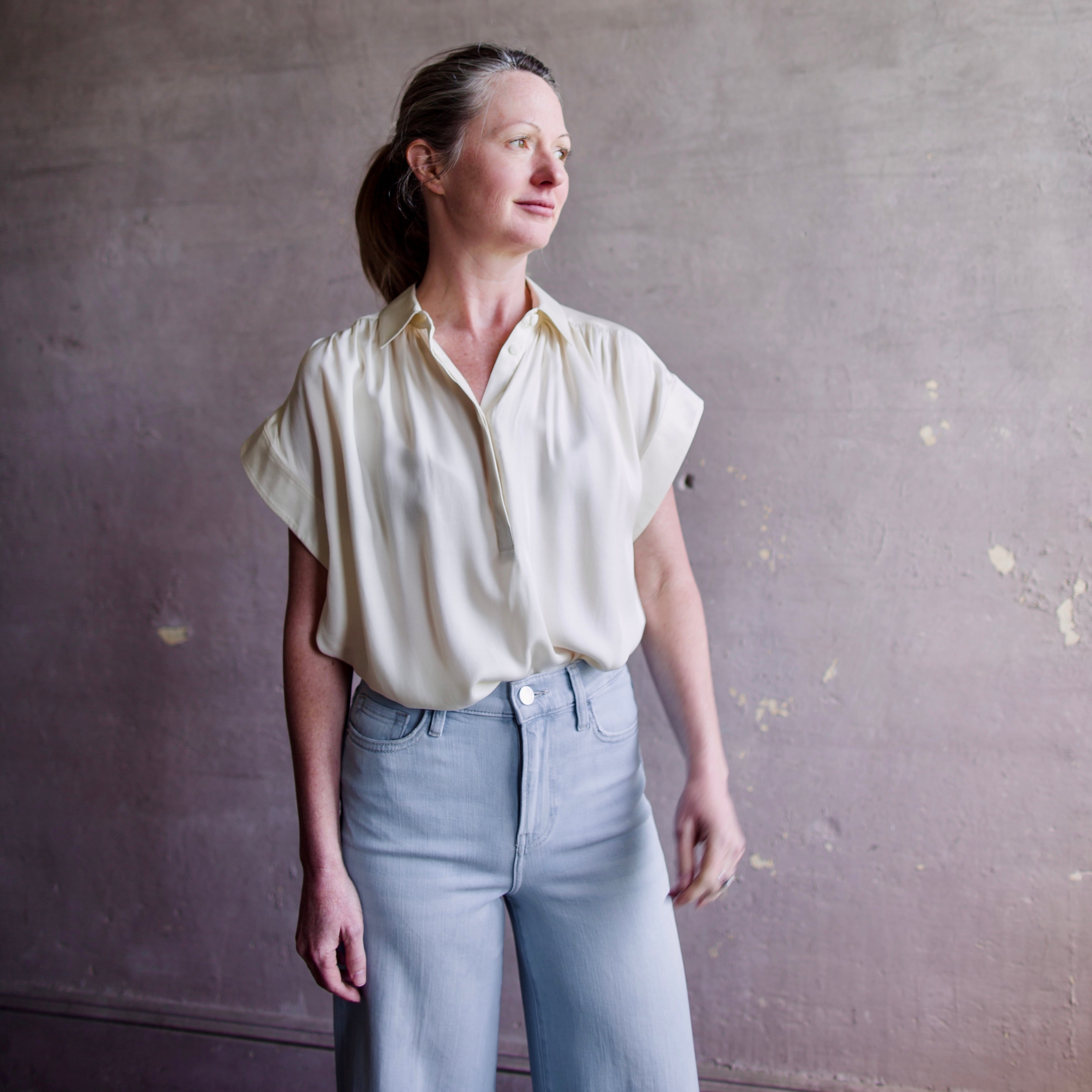 Image featuring a woman wearing the Rag & Bone Robin silk blouse in cream with a collared neckline and button down front. 