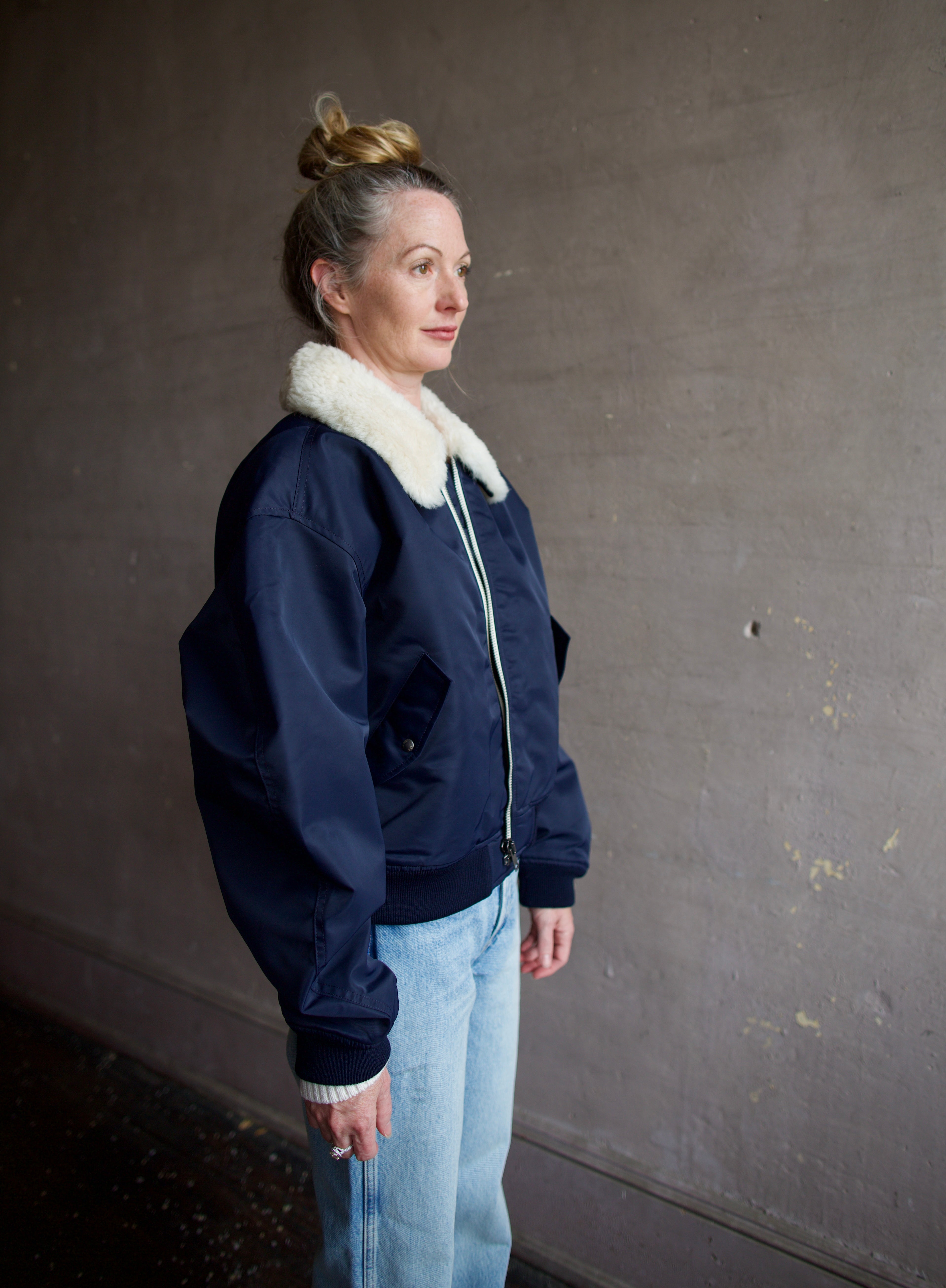 Image featuring a woman wearing the navy blue Bomber Jacket by Re/Done with a cream shearling collar and goat suede undercollar.