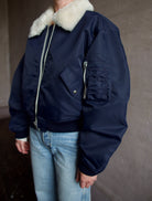 Image featuring a woman wearing the navy blue Bomber Jacket by Re/Done with a cream shearling collar and goat suede undercollar.