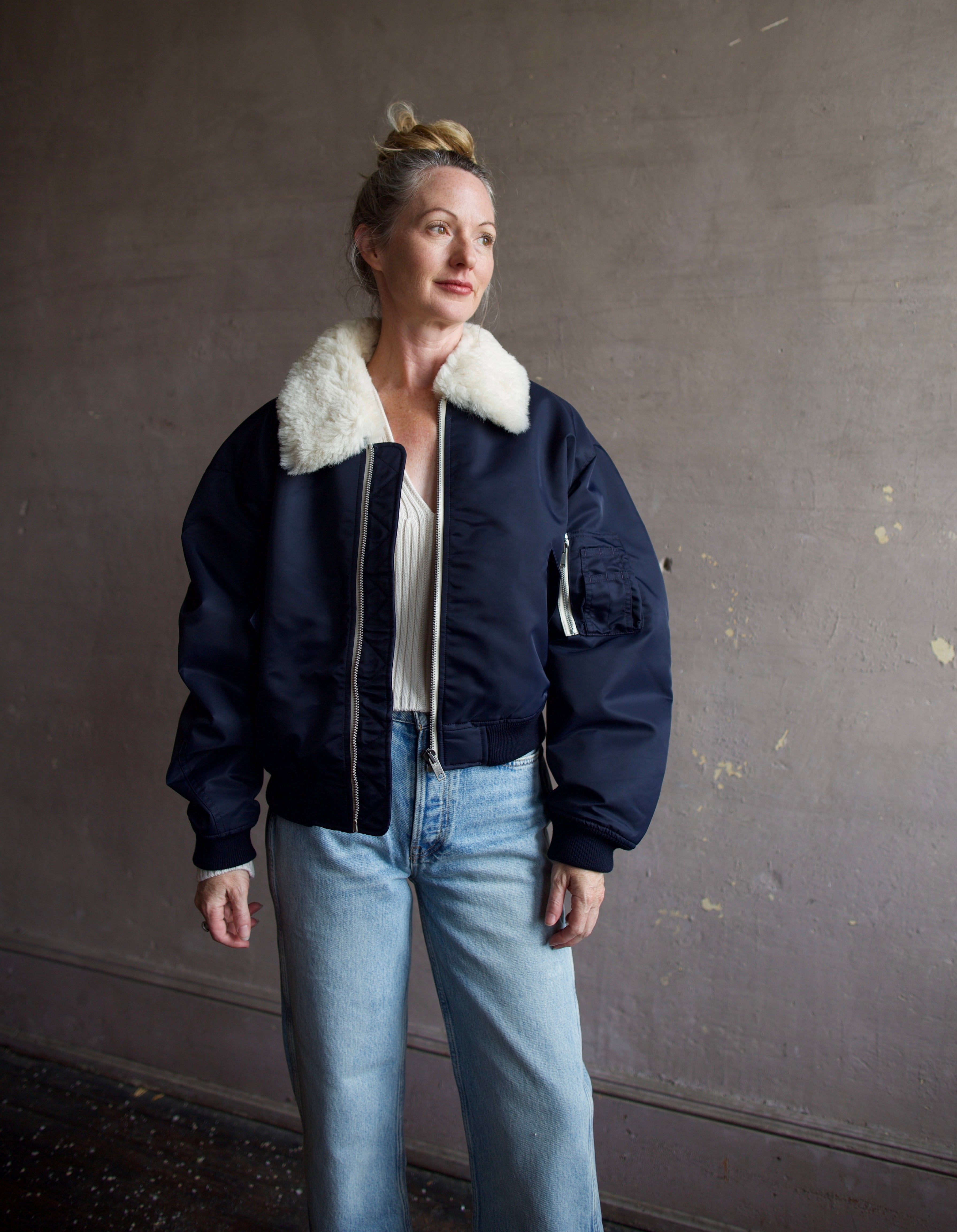 Image featuring a woman wearing the navy blue Bomber Jacket by Re/Done with a cream shearling collar and goat suede undercollar.