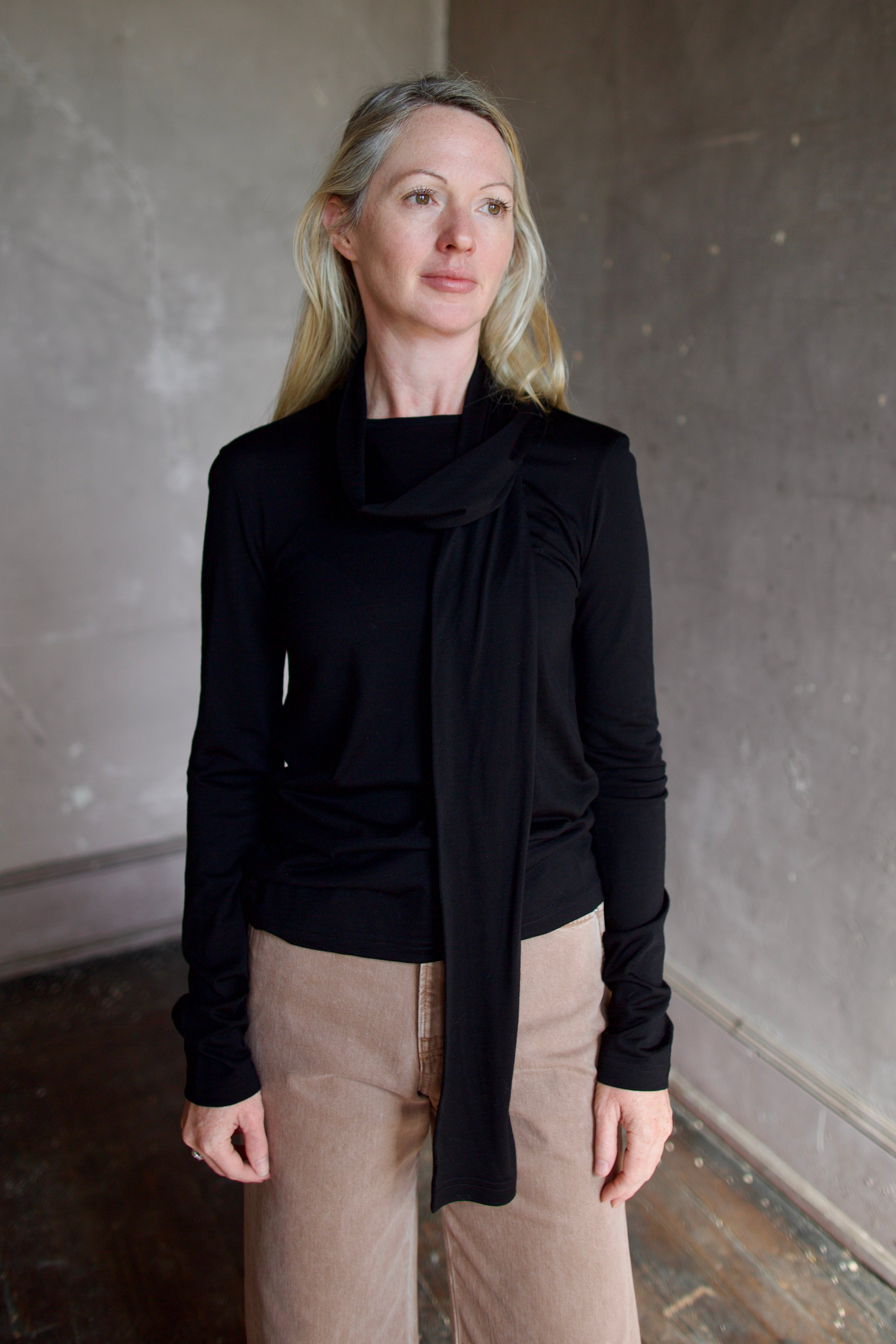 Model wearing a premium merino wool black top by luxury Amsterdam designer Rohe with integrated scarf for an quality elevated basic