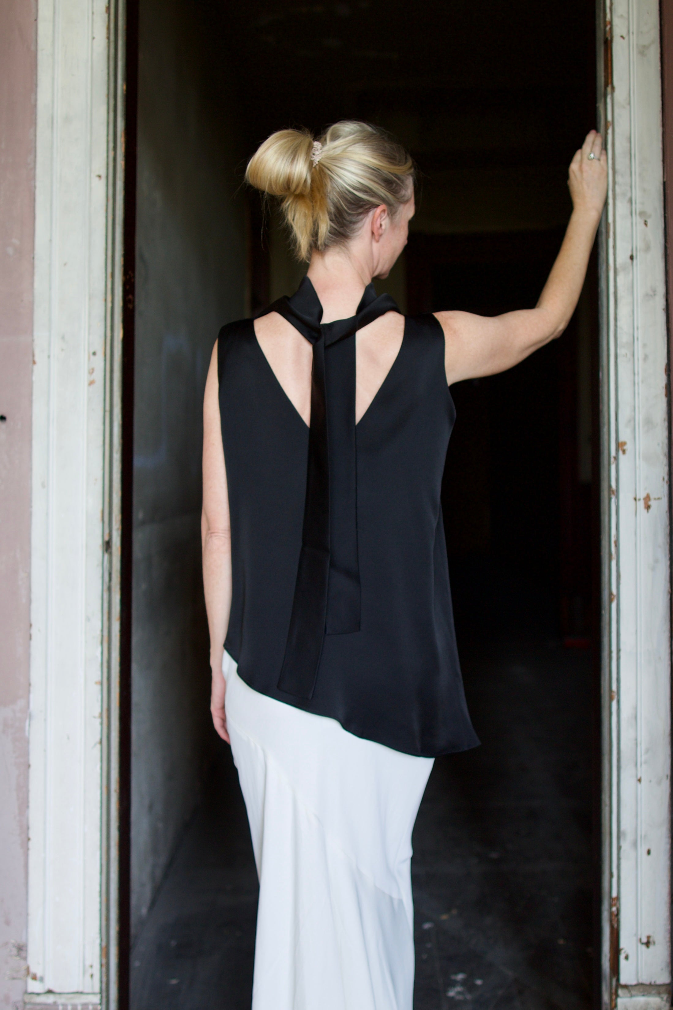 Model wearing black sleeveless satin top with expertly crafted draping and attached tie by luxury modern designer Rohe 