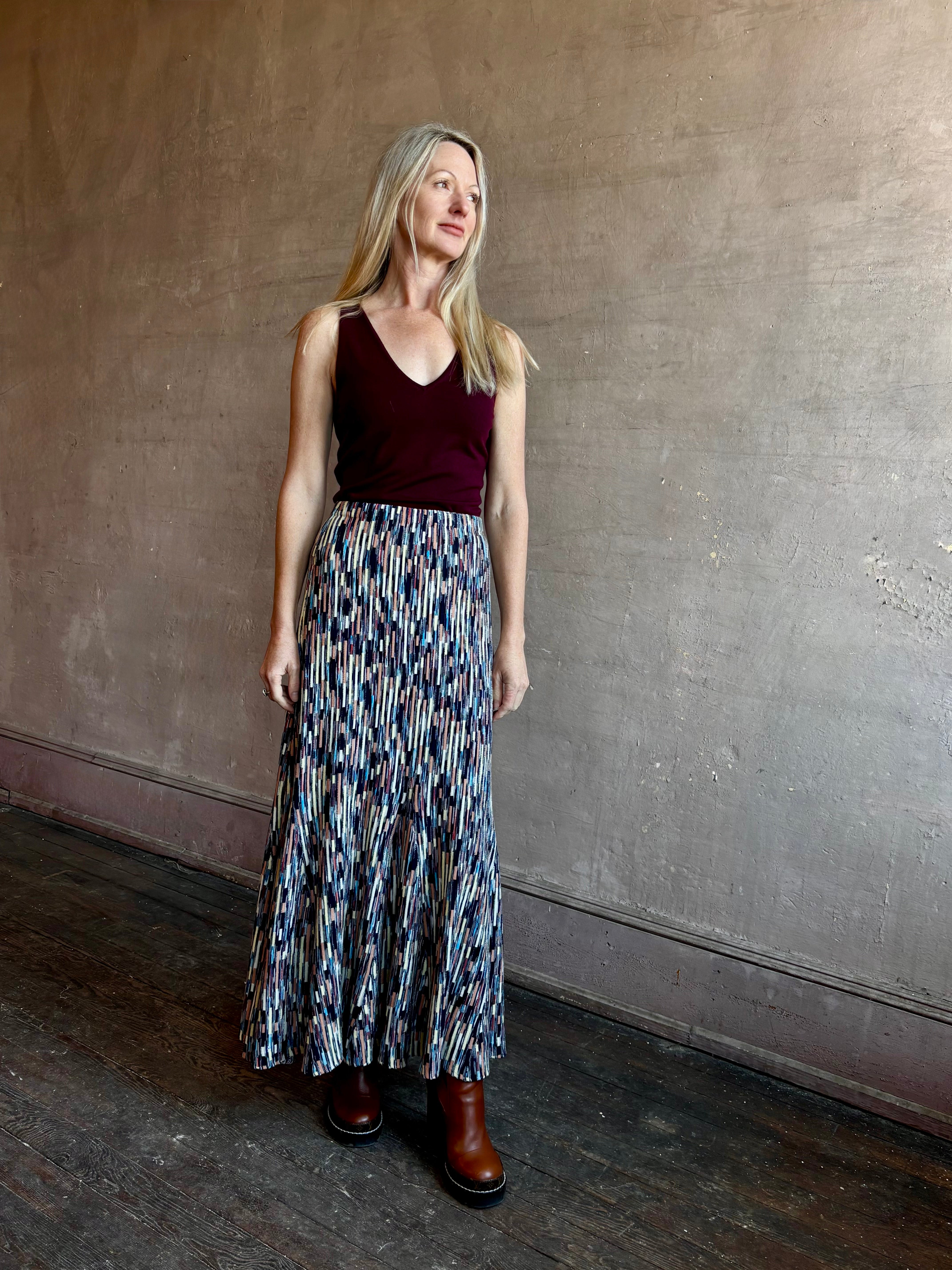 Image of mature woman wearing a rich burgundy Sablyn Addyson V-neck layering tank top with Ulla Johnson Merceline Multi-color long knit skirt in oasis.