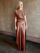 Woman wearing luxury SABLYN Grace Scallop Trim Bias Cut silk Maxi Pull On Skirt in a neutral copper color with matching sweater set