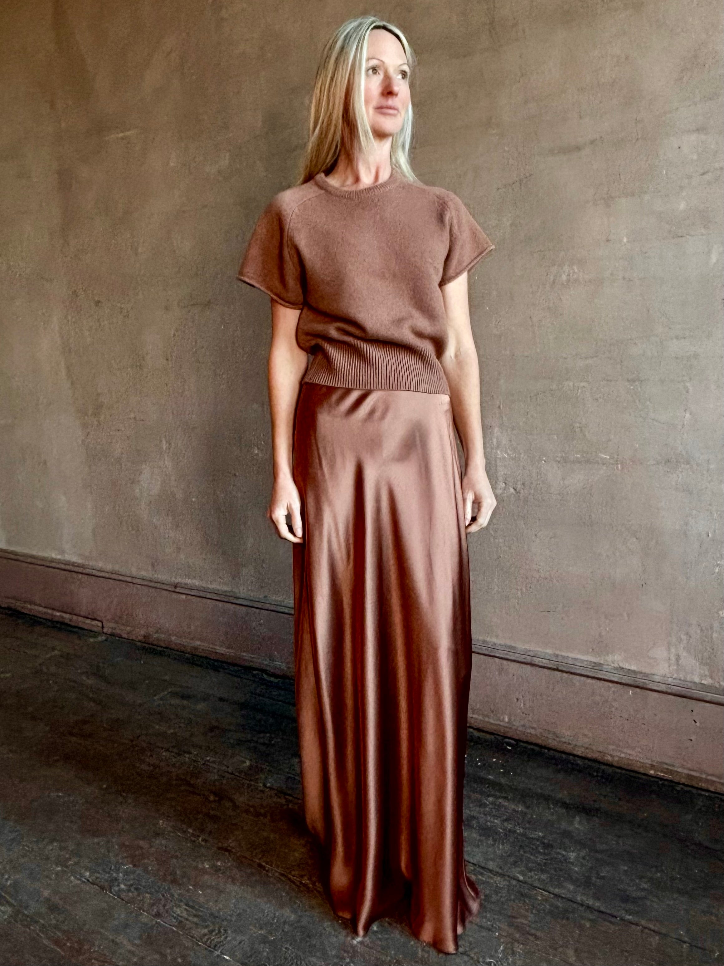 Woman wearing luxury SABLYN Grace Scallop Trim Bias Cut silk Maxi Pull On Skirt in a neutral copper color with matching sweater set