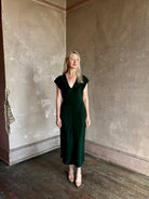 Mature woman wearing Sablyn Inez draped silk V-neck dark green midi dress with short cap sleeves made in USA