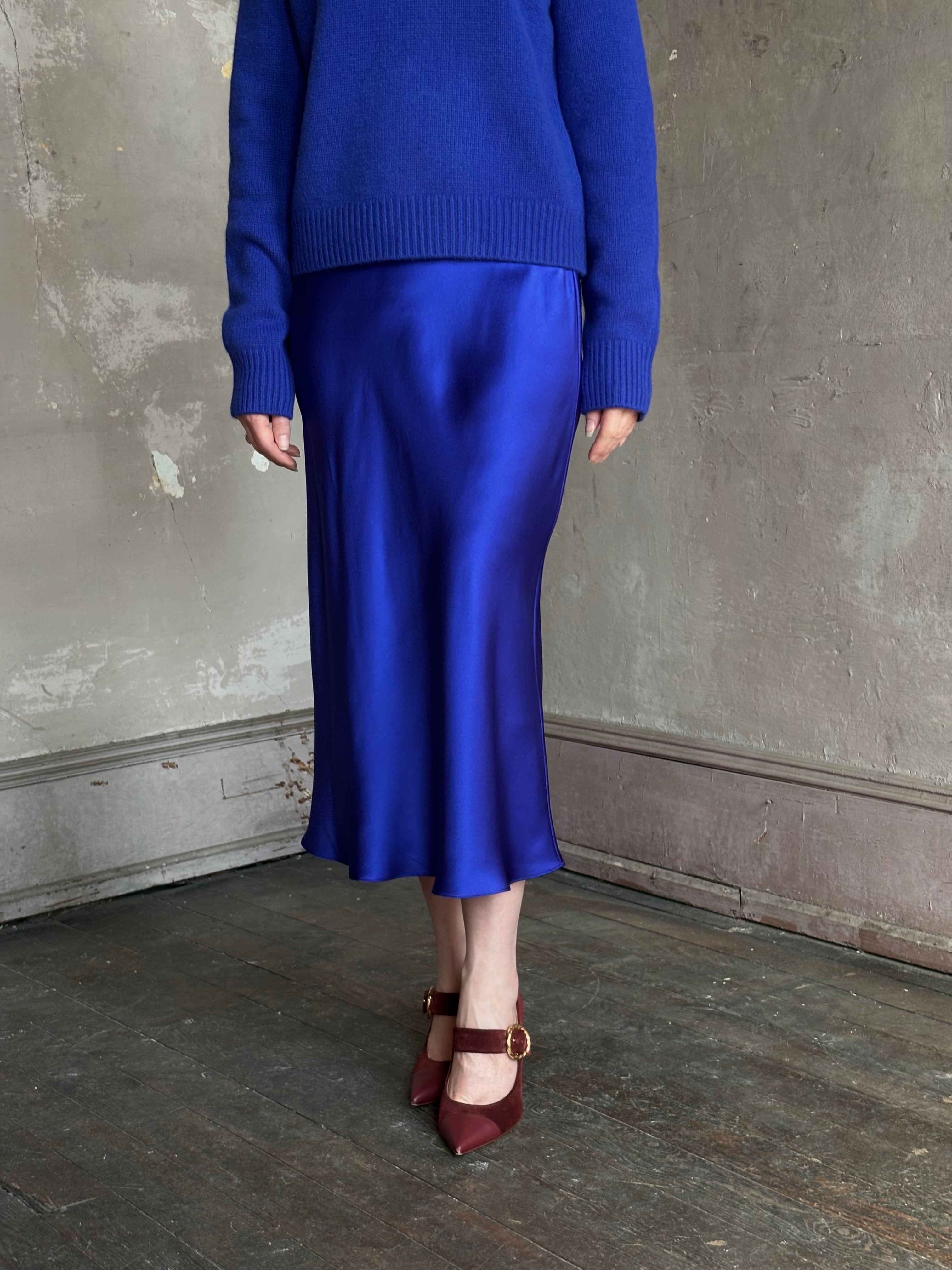 Mature woman wearing a vibrant royal blue silk bias cut midi skirt and matching cashmere knit sweater set