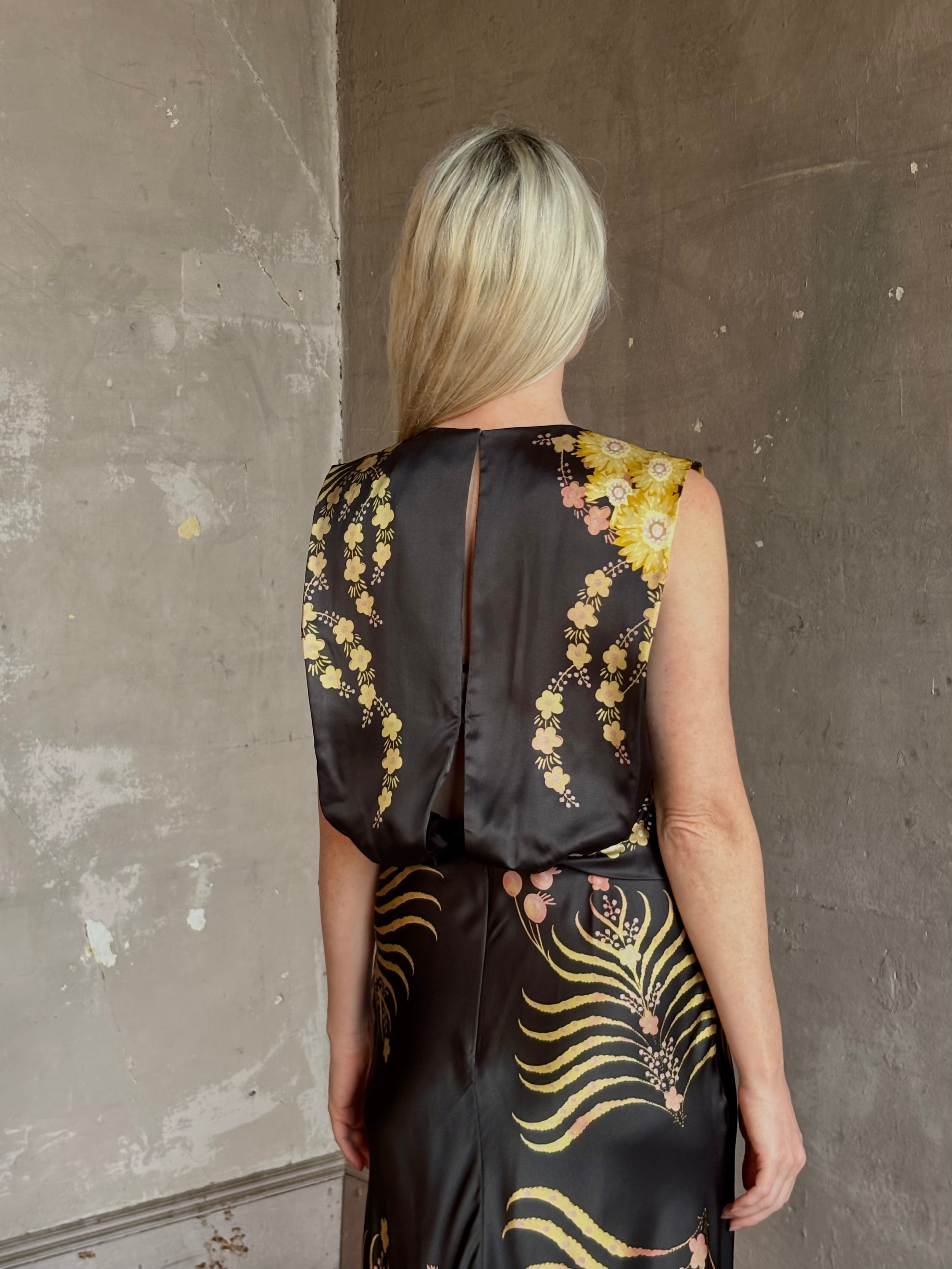 Mature woman wearing Saloni Gwen Dress in Golden Palm semi-open back gathered waist black with yellow and pink print evening gown