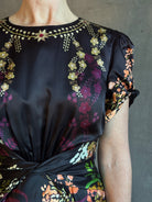 Mature woman wearing Saloni's Gwen C Dress in Equinox Plmt silk blend fit-and-flare silhouette cummerbund waist. Botanical, structured occasion elegance.