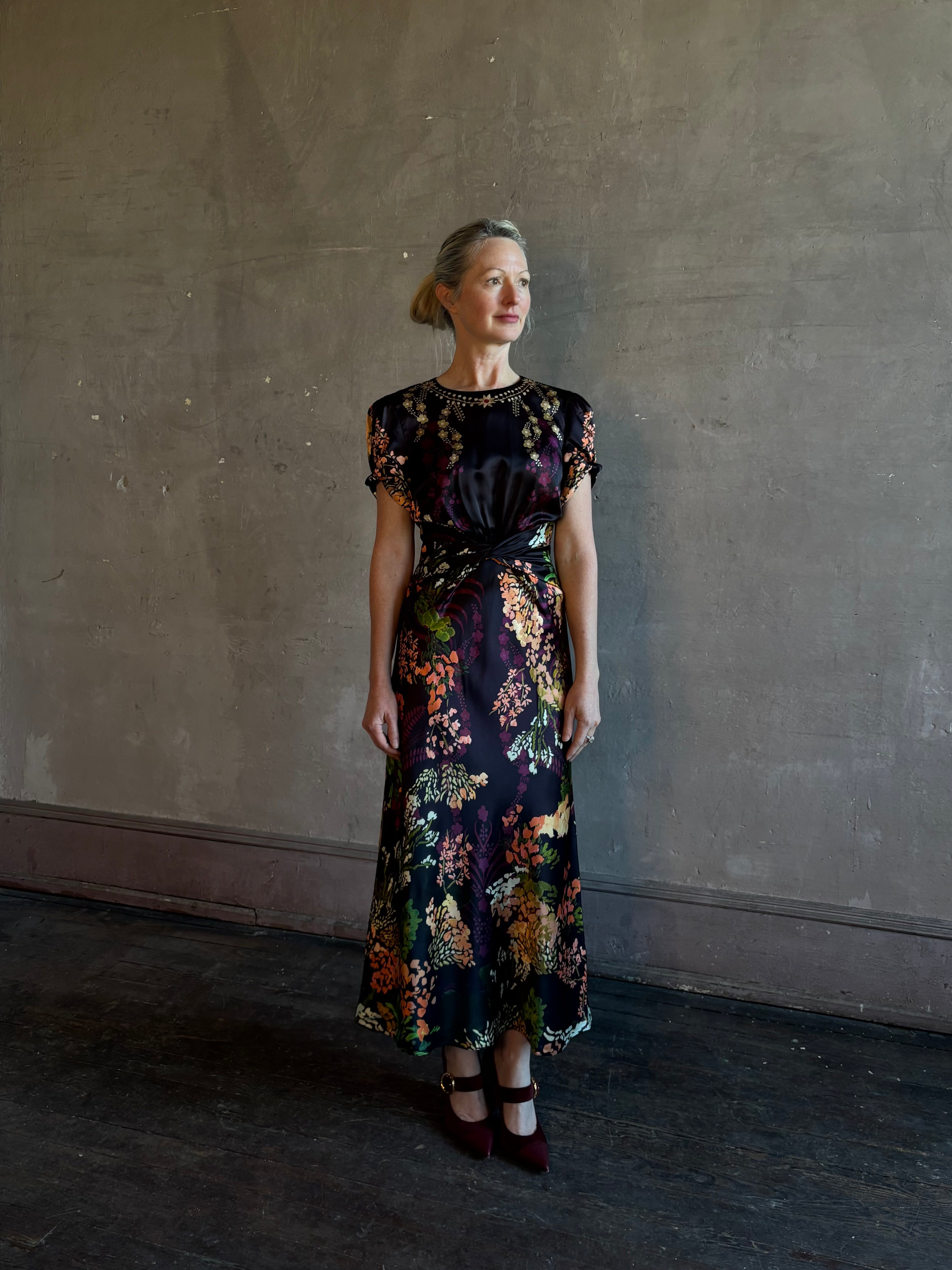 Mature woman wearing Saloni's Gwen C Dress in Equinox Plmt silk blend fit-and-flare silhouette cummerbund waist. Botanical, structured occasion elegance.