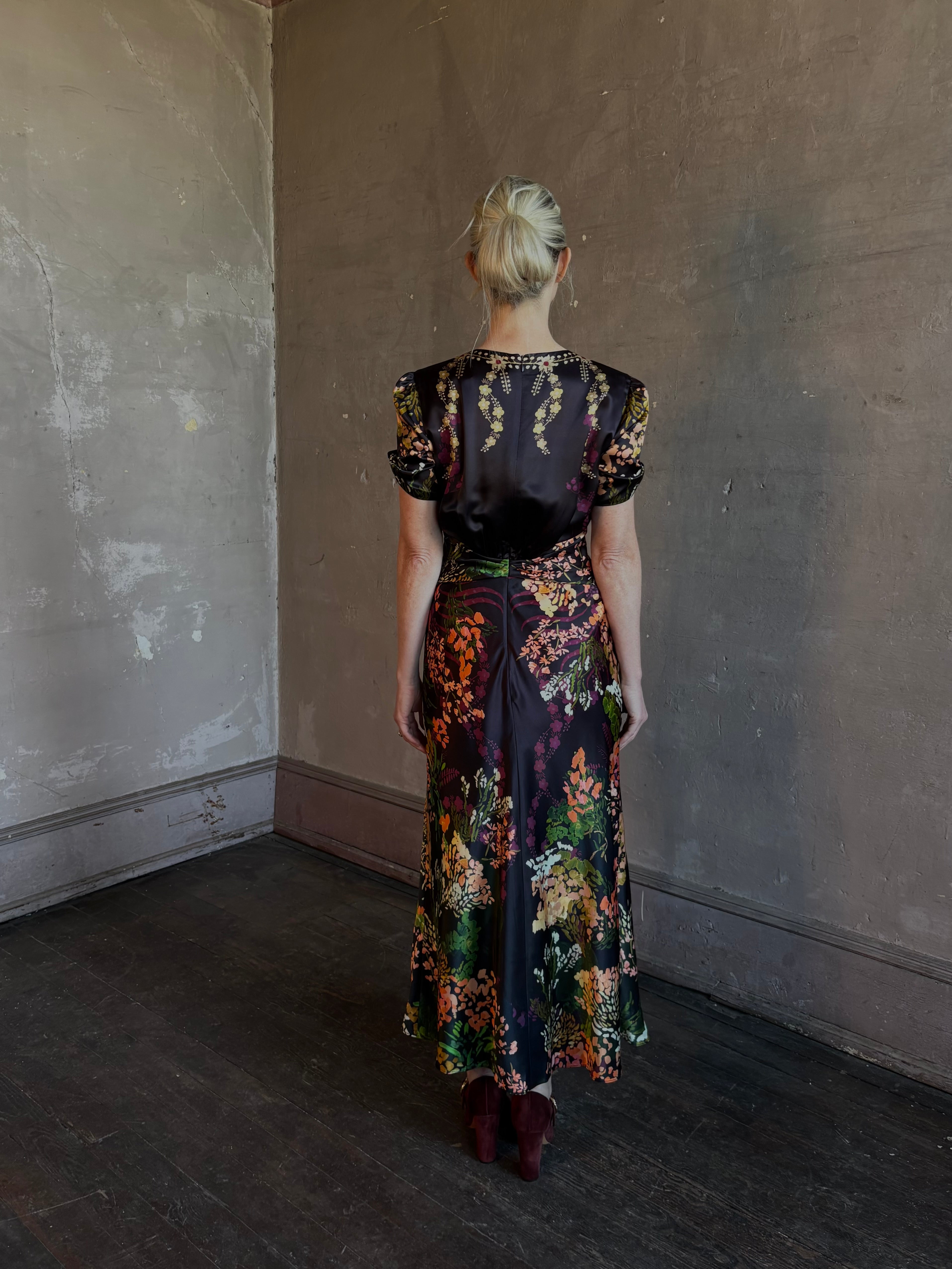 Mature woman wearing Saloni's Gwen C Dress in Equinox Plmt silk blend fit-and-flare silhouette cummerbund waist. Botanical, structured occasion elegance.