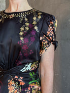 Mature woman wearing Saloni's Gwen C Dress in Equinox Plmt silk blend fit-and-flare silhouette cummerbund waist. Botanical, structured occasion elegance.