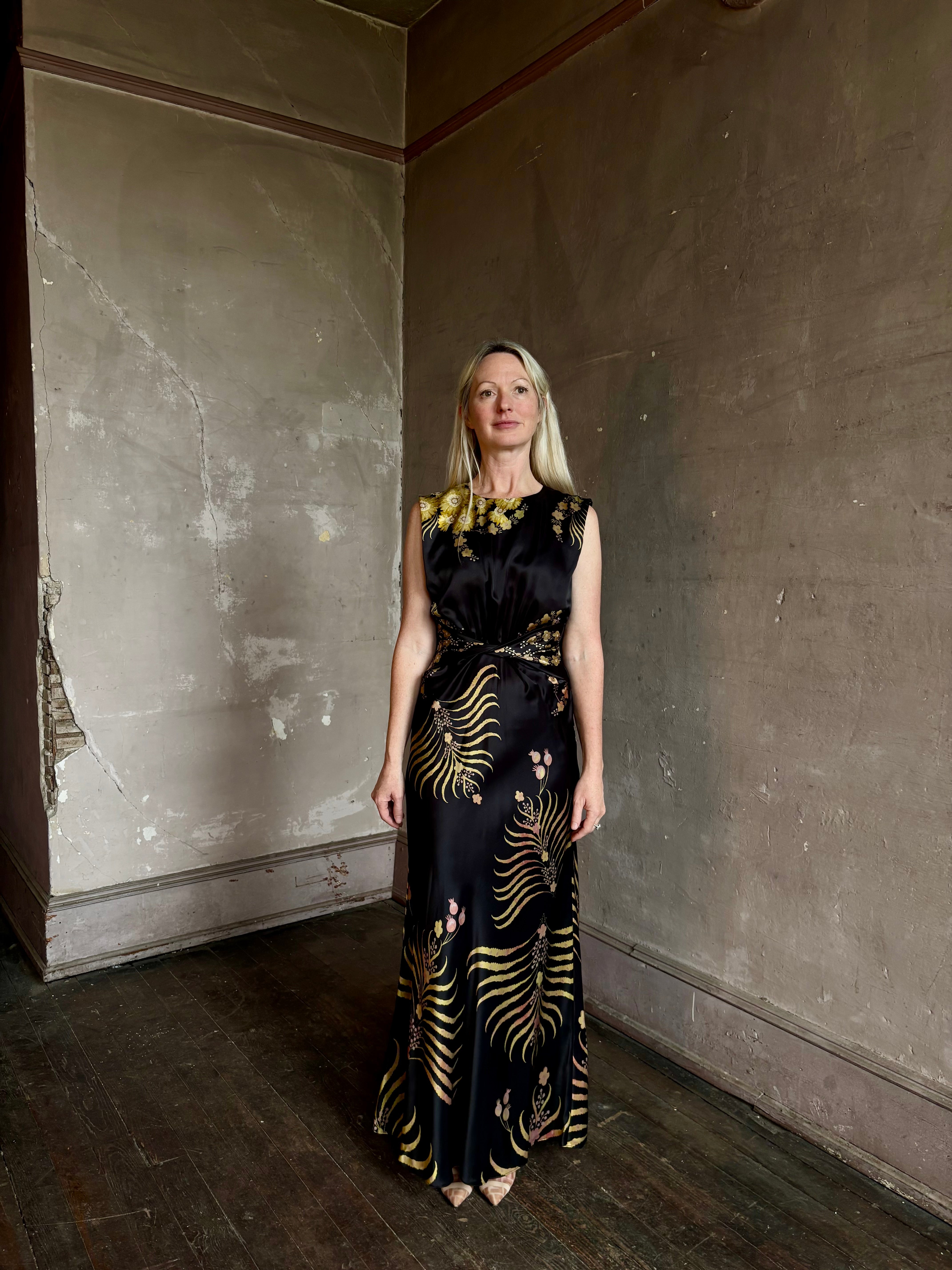 Mature woman wearing Saloni Gwen Dress in Golden Palm semi-open back gathered waist black with yellow and pink print evening gown