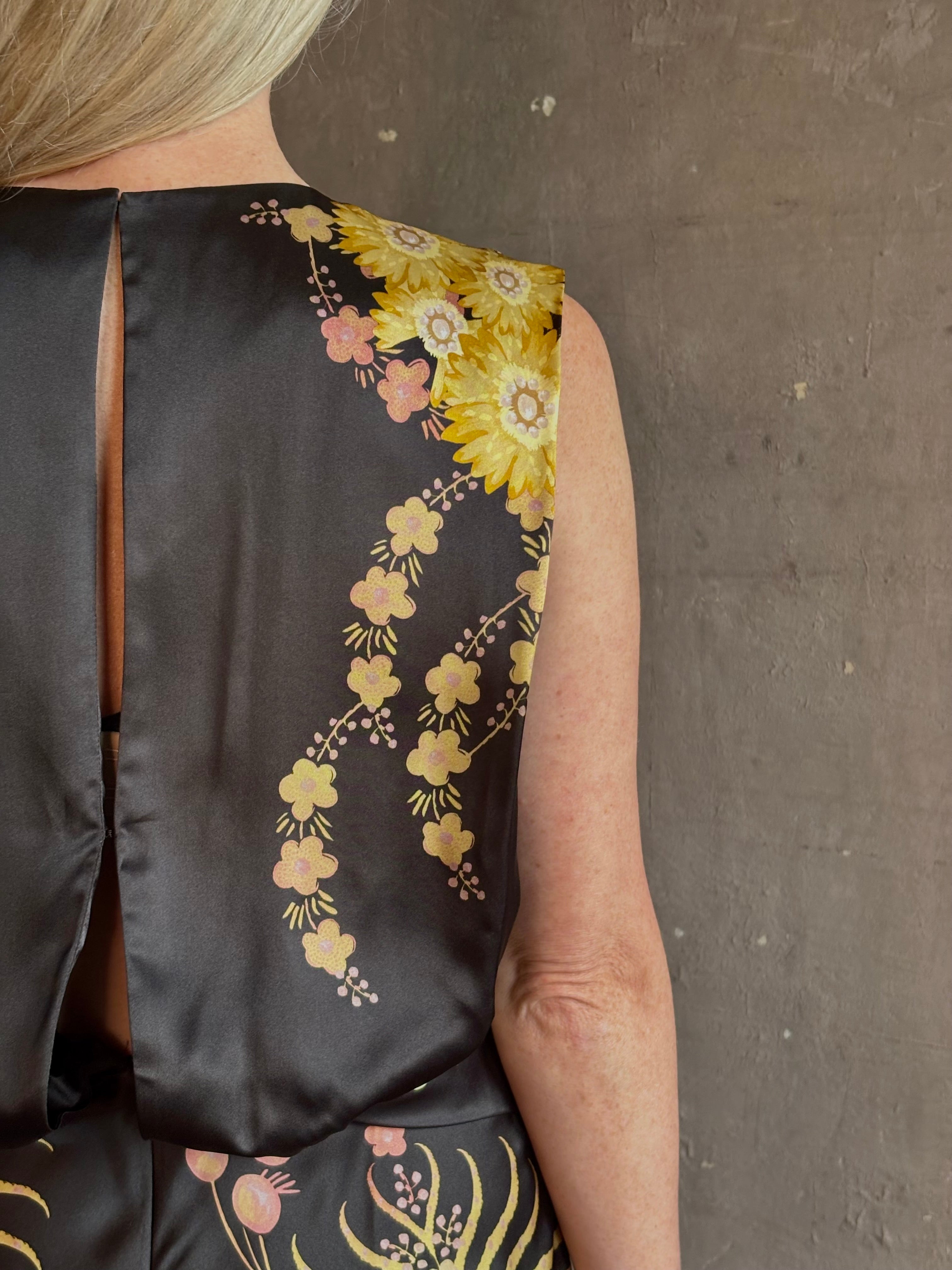 Mature woman wearing Saloni Gwen Dress in Golden Palm semi-open back gathered waist black with yellow and pink print evening gown