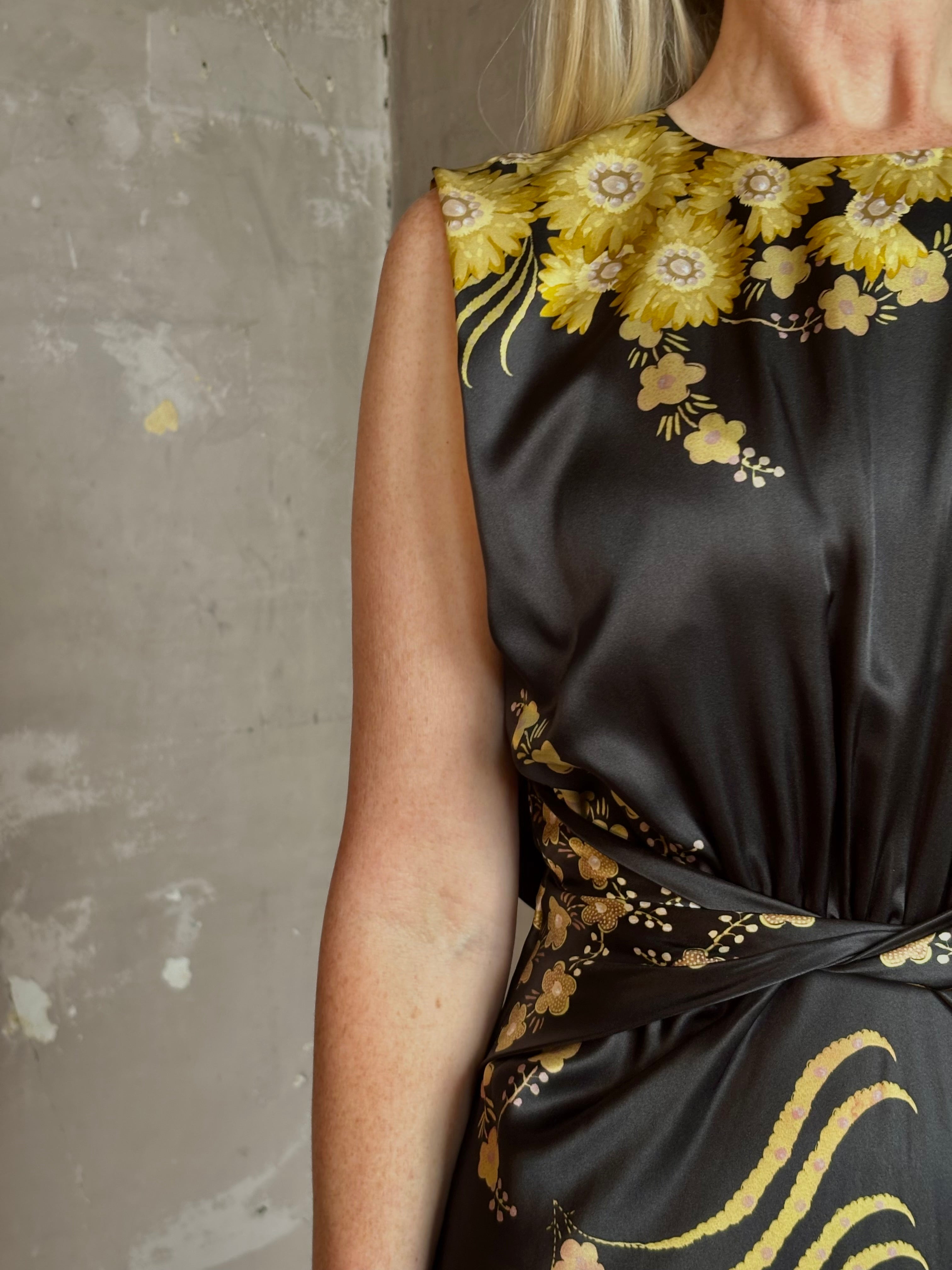 Mature woman wearing Saloni Gwen Dress in Golden Palm semi-open back gathered waist black with yellow and pink print evening gown