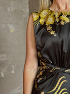 Mature woman wearing Saloni Gwen Dress in Golden Palm semi-open back gathered waist black with yellow and pink print evening gown