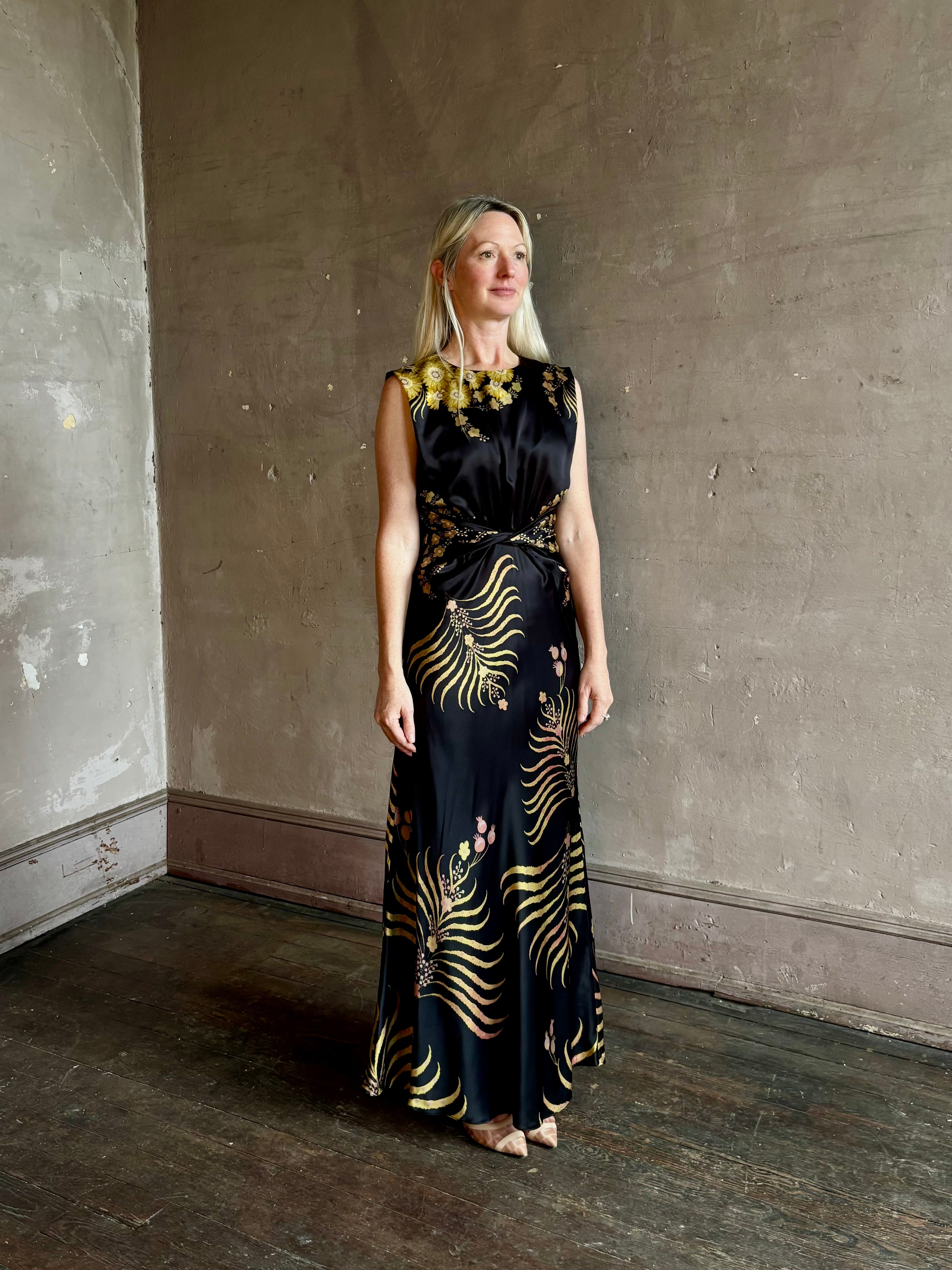 Mature woman wearing Saloni Gwen Dress in Golden Palm semi-open back gathered waist black with yellow and pink print evening gown