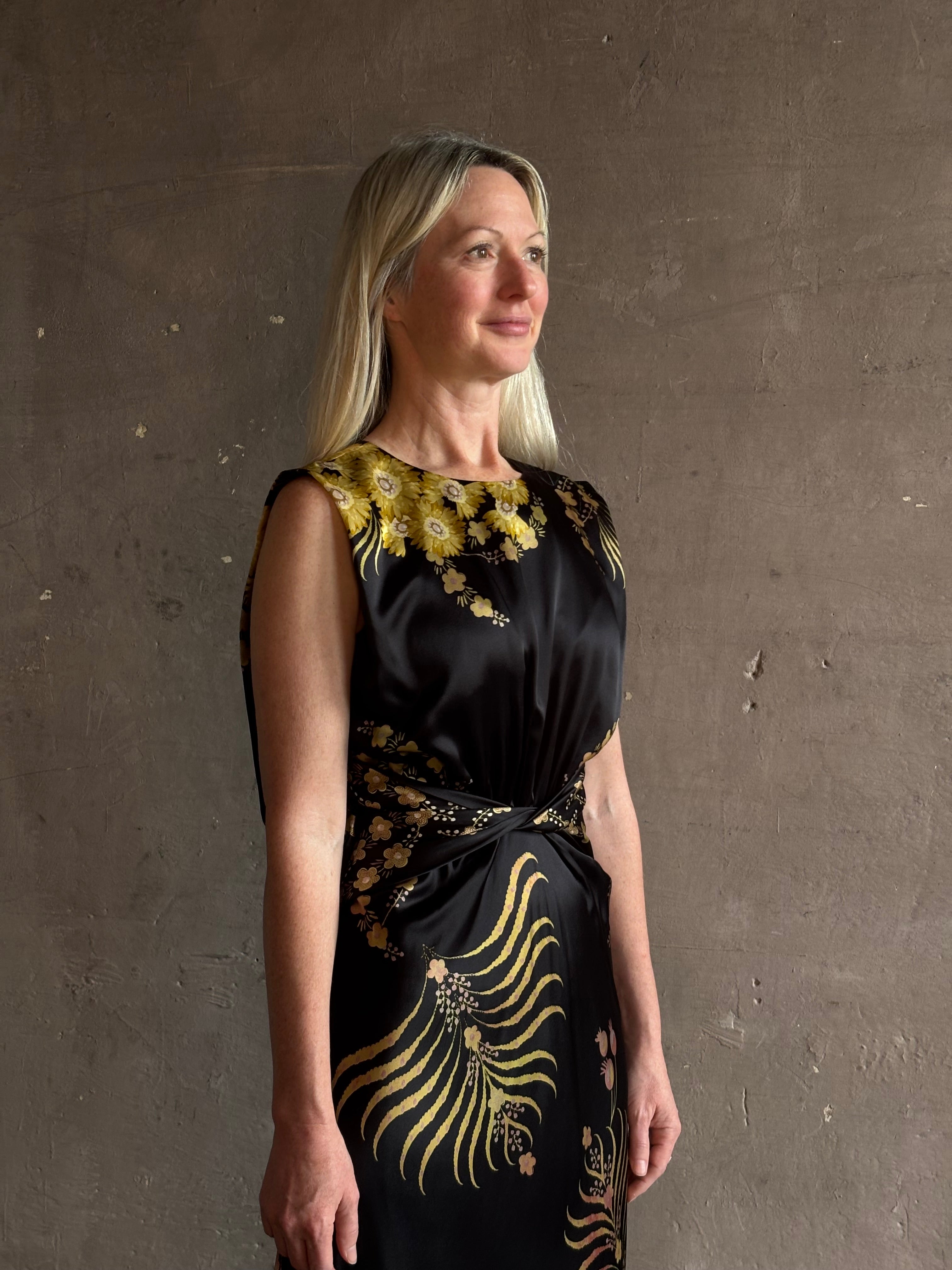 Mature woman wearing Saloni Gwen Dress in Golden Palm semi-open back gathered waist black with yellow and pink print evening gown