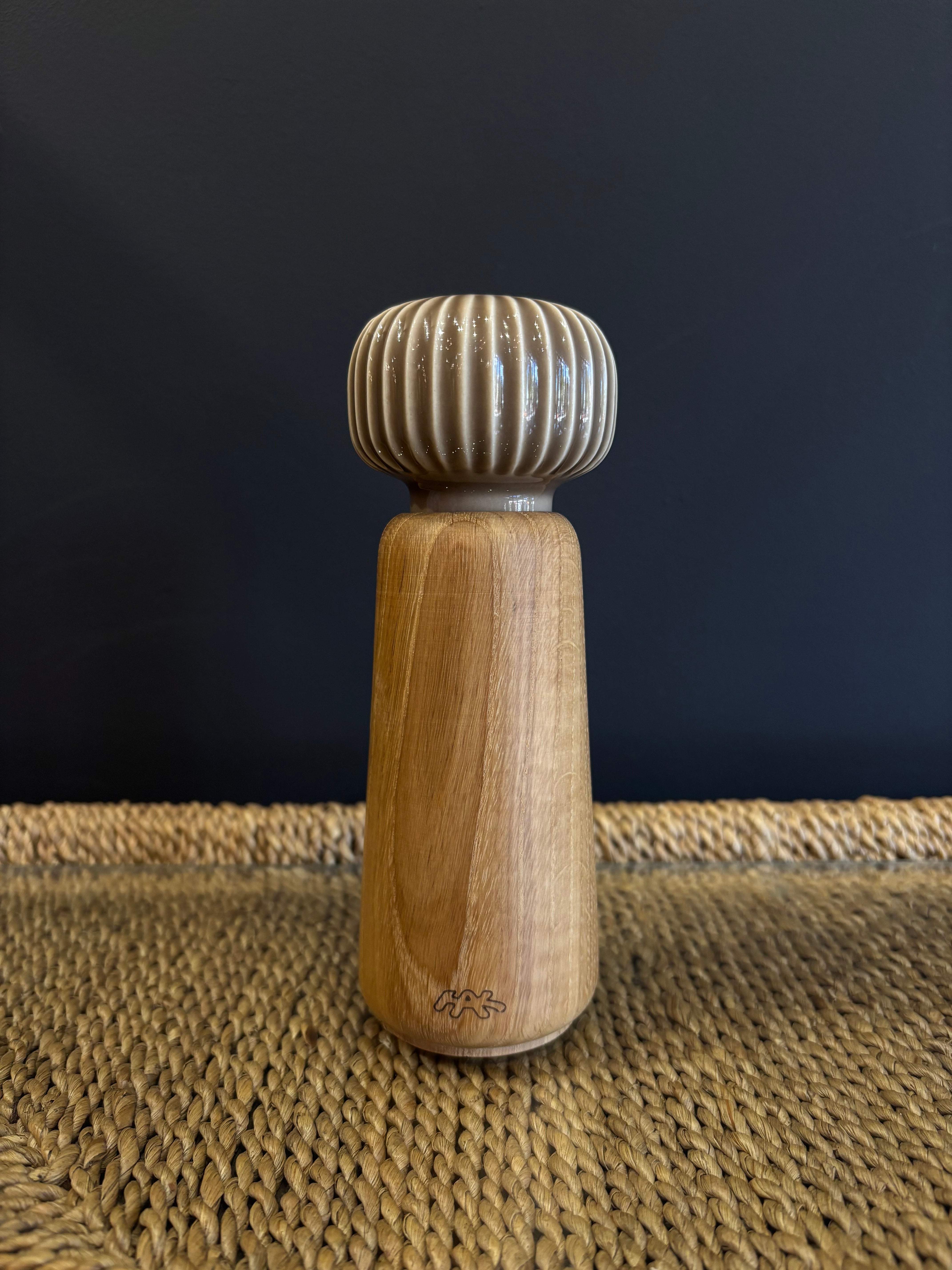A wooden spice grinder with a neutral taupe beige ribbed ceramic top and a natural finish oak wood body