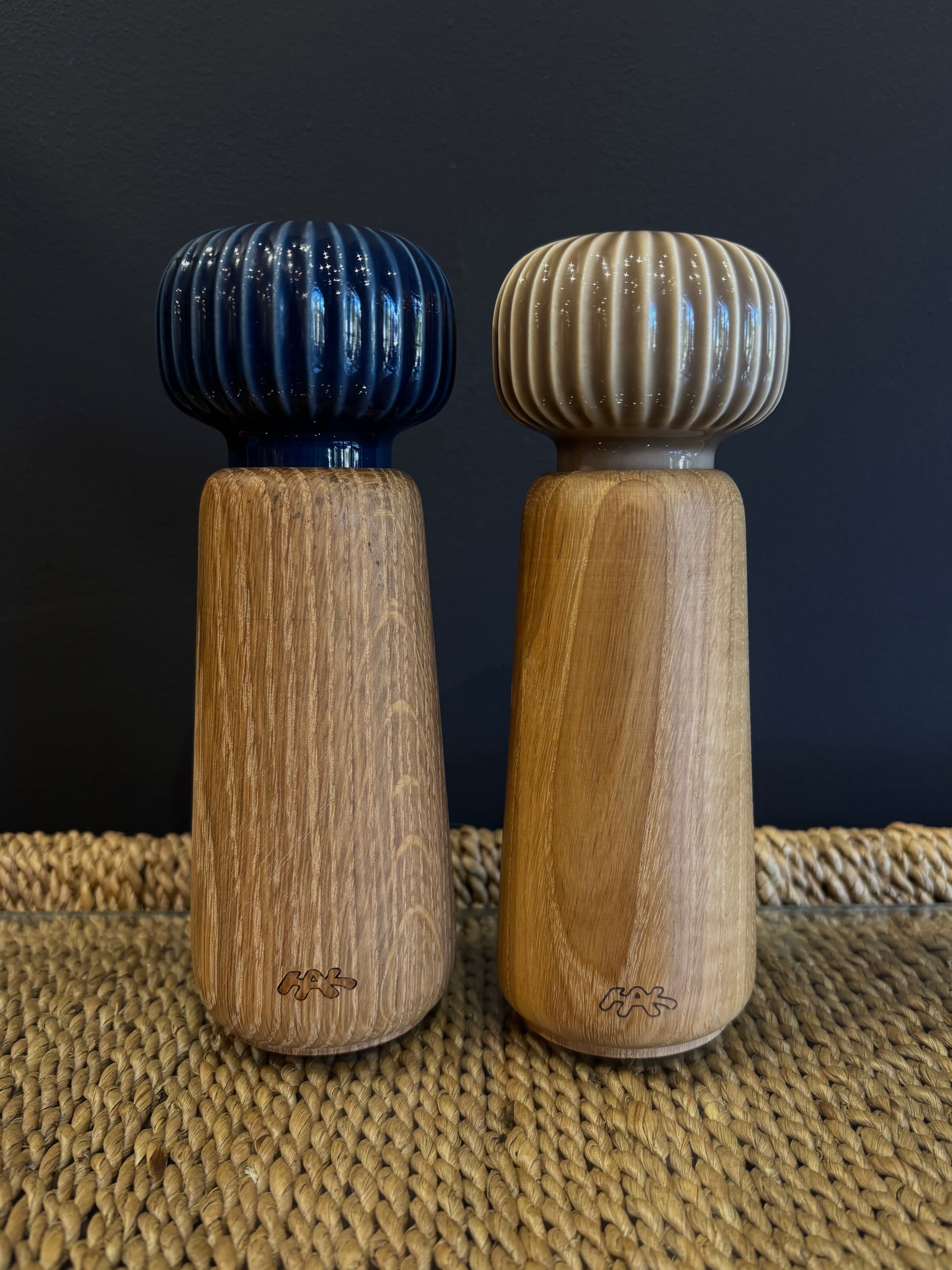 A wooden spice grinder set with a neutral taupe beige and navy blue ribbed ceramic top and a natural finish oak wood body