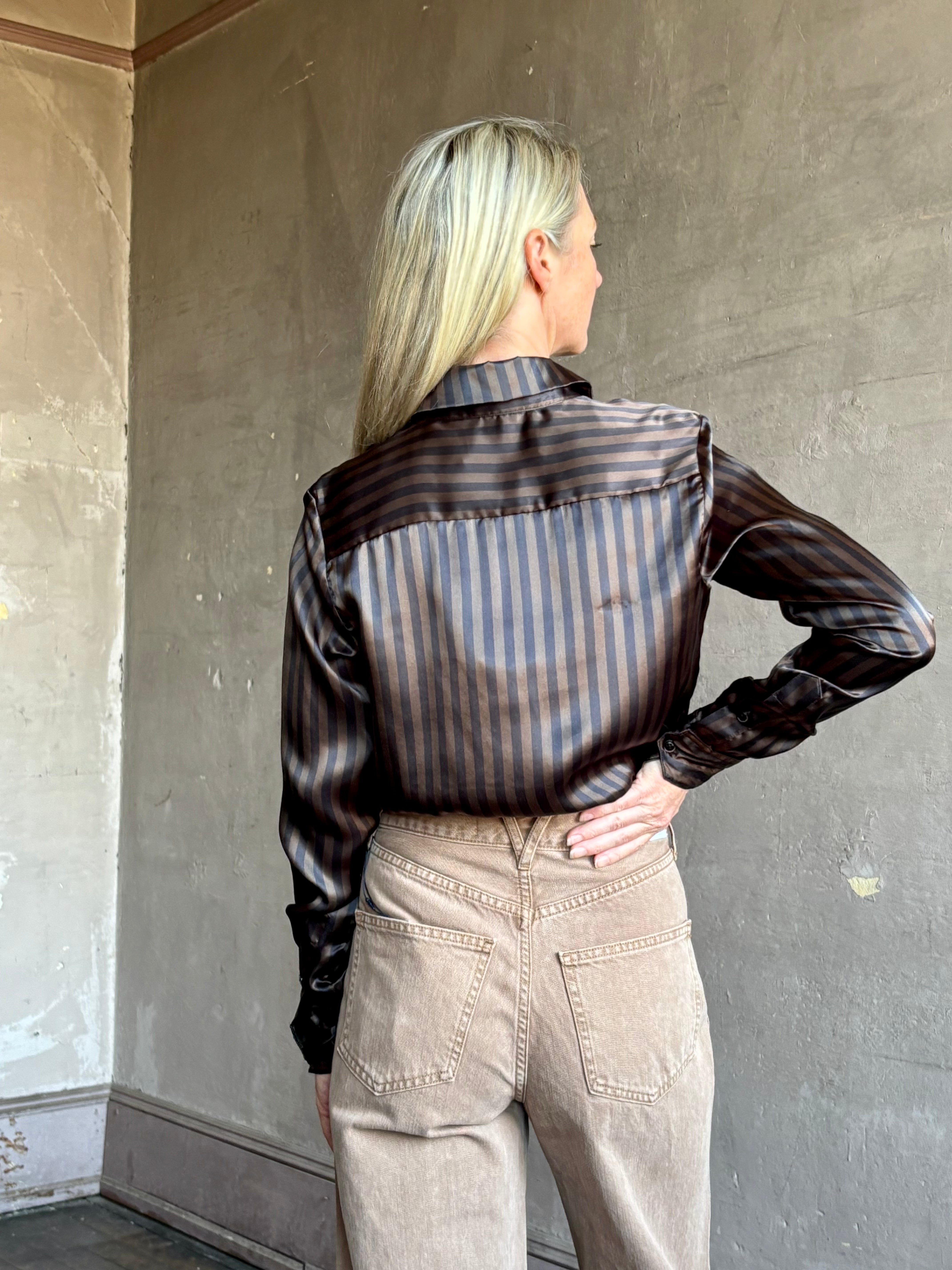 Image of woman wearing luxury brand SPRWMN Fonda silk button up shirt in a black and brown stripe modern classic.