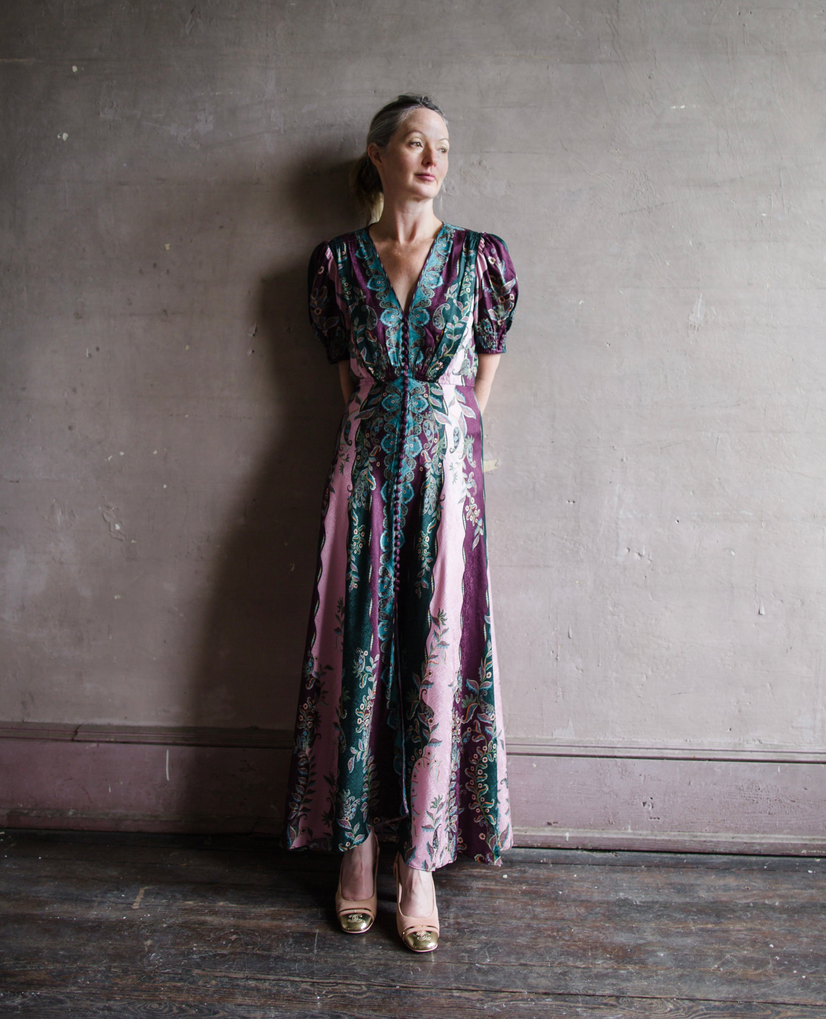 Image featuring a woman wearing the Lea Long silk Dress by Saloni with a v neckline, button front, puff short sleeves and a tailored waist in stripe plum, teal, & pink.