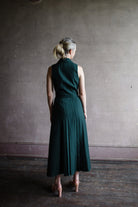 Image featuring a woman wearing the Livi wool blend dress by Saloni with a v neckline, button front and  accordion pleating in forest green.