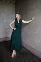 Image featuring a woman wearing the Livi wool blend dress by Saloni with a v neckline, button front and  accordion pleating in forest green.