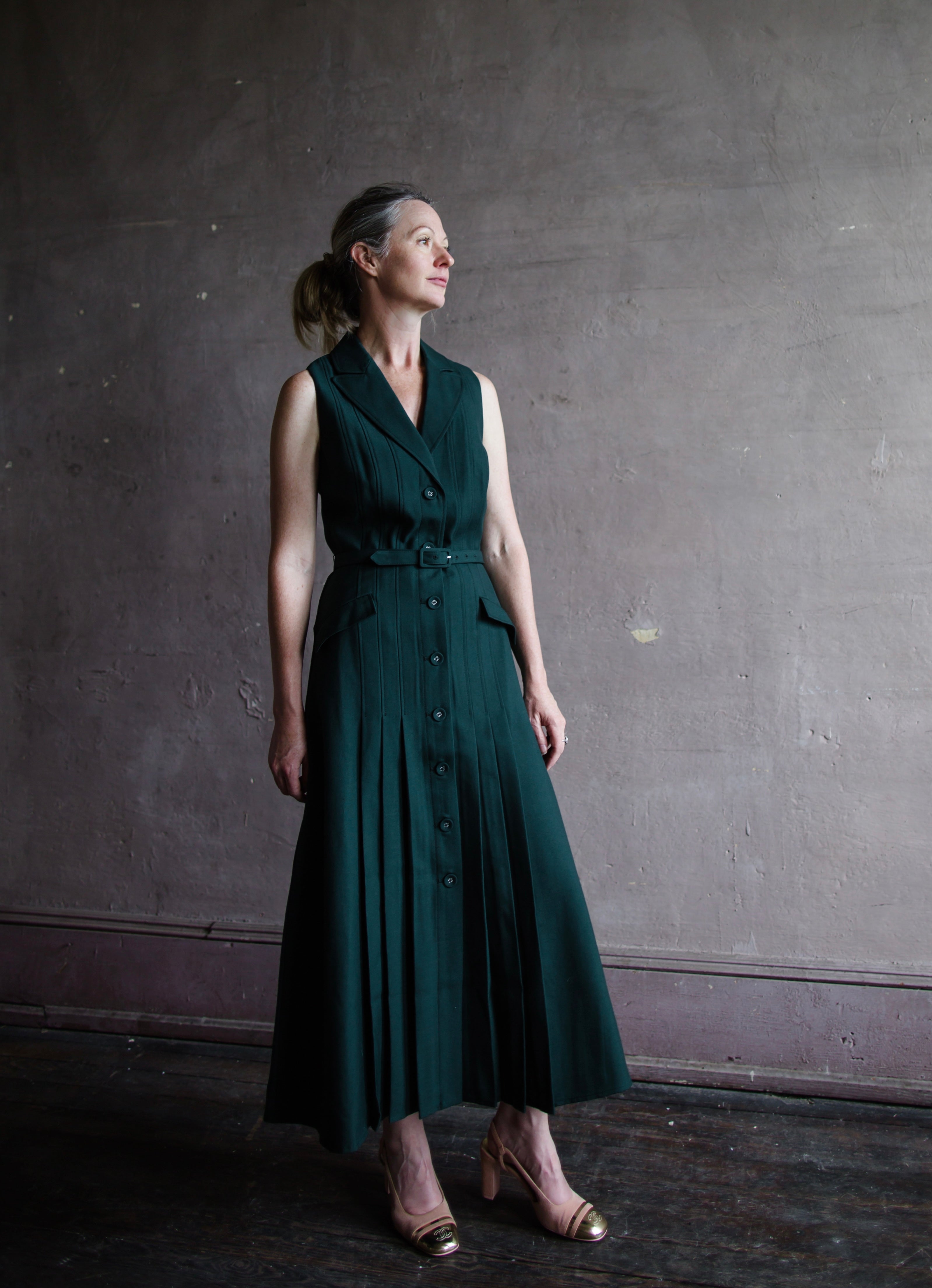 Image featuring a woman wearing the Livi wool blend dress by Saloni with a v neckline, button front and  accordion pleating in forest green.