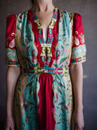 Image featuring a woman wearing the Tabitha silk dress by Saloni with a v neckline, puff short sleeves and a cinched waist in red, yellow, and aqua floral print.