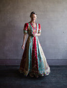 Image featuring a woman wearing the Tabitha silk dress by Saloni with a v neckline, puff short sleeves and a cinched waist in red, yellow, and aqua floral print.