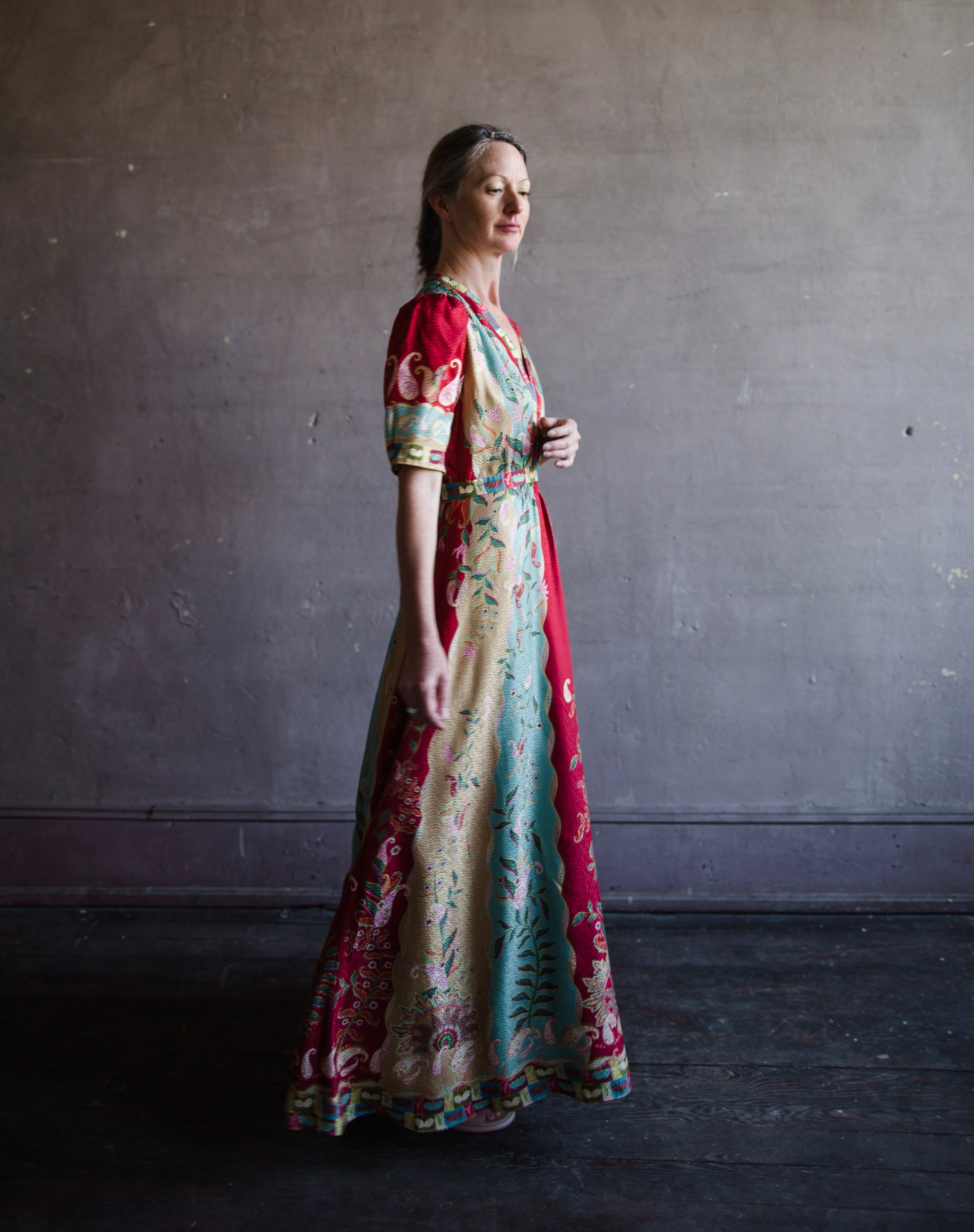 Image featuring a woman wearing the Tabitha silk dress by Saloni with a v neckline, puff short sleeves and a cinched waist in red, yellow, and aqua floral print.