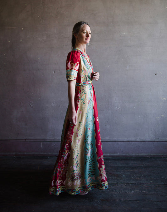 Image featuring a woman wearing the Tabitha silk dress by Saloni with a v neckline, puff short sleeves and a cinched waist in red, yellow, and aqua floral print.