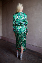Mature woman wearing Saloni Mya silk long sleeve green floral midi dress with embellished broach detail at waist, long sleeves, and V-neck