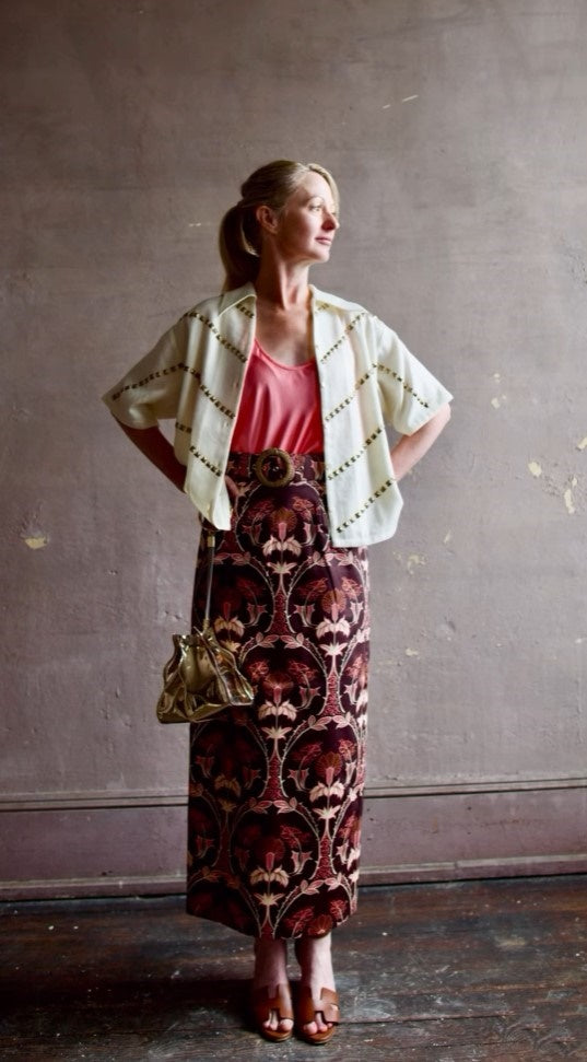 Image of woman wearing Cara Cara Blaze Skirt in Arcada Chocolate cotton-spandex construction with elegant Morris floral print, raffia belt, and straight hem