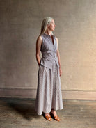 Mature woman wearing the Hannah maxi shirt dress from designer Tanya Taylor rendered in a brown and white stripe and crafted from 100% cotton poplin with a very classy flattering waistline that doesn't stick to body, sleeveless with a collar for a timeless tailored classic dress