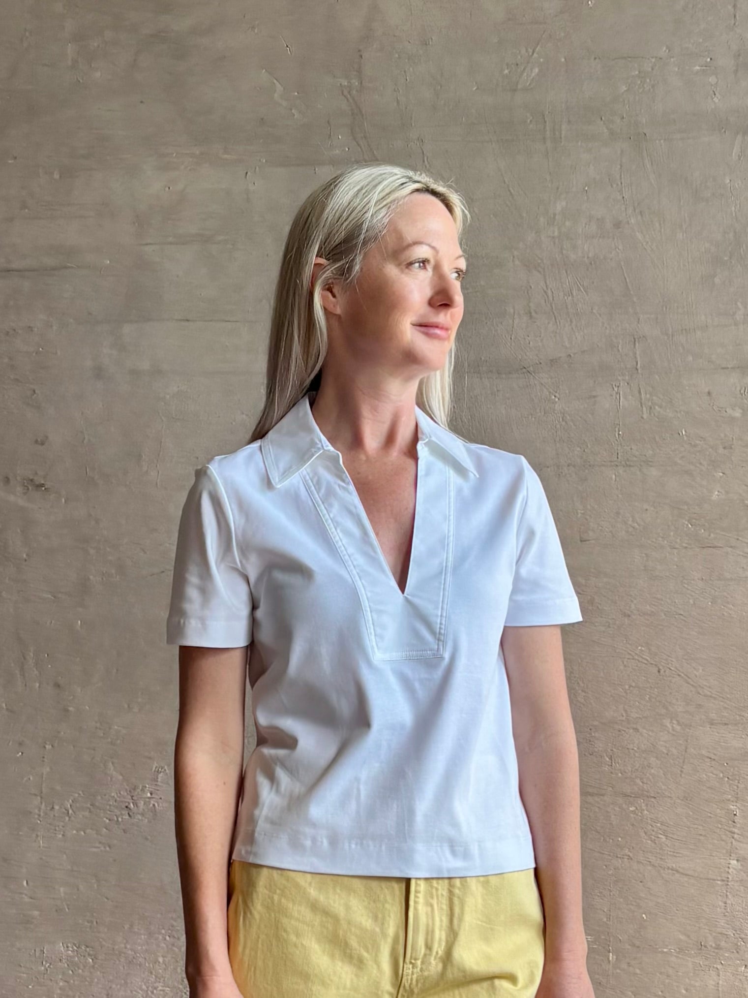 Mature woman wearing timeless white Melanie Top from Tanya Taylor crafted from 100% organic cotton jersey with v-neck and short sleeves in effortless relaxed fit for an elevated waredrobe staple